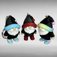 Three gnome-shaped keychains in black with different colored hats (blue/white gradient and black, shimmer red and black, and pastel rainbow gradient and black) with shoes the same color as the hats on a gray background