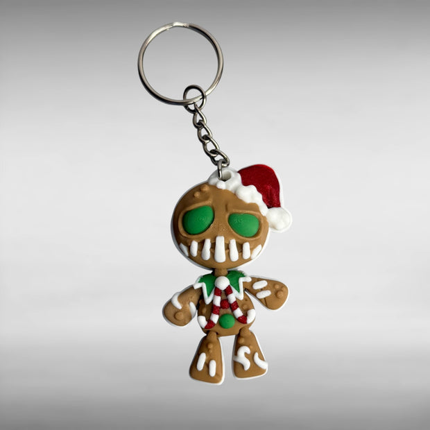 Keychain shaped like a gingerbread man with green eyes, candy cane shaped bowtie, and a Santa hat on a gray background 