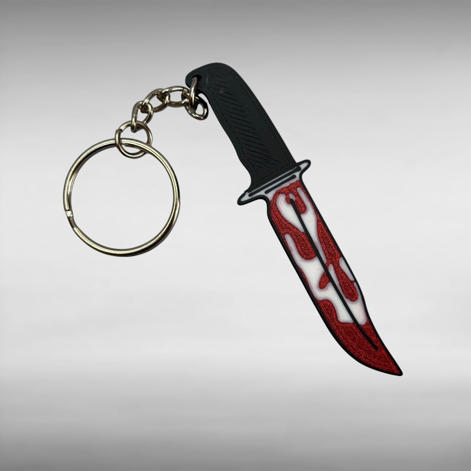 Keychain resembling a knife with a blood-stained blade on a gray background