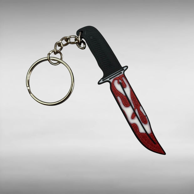 Keychain resembling a knife with a blood-stained blade on a gray background