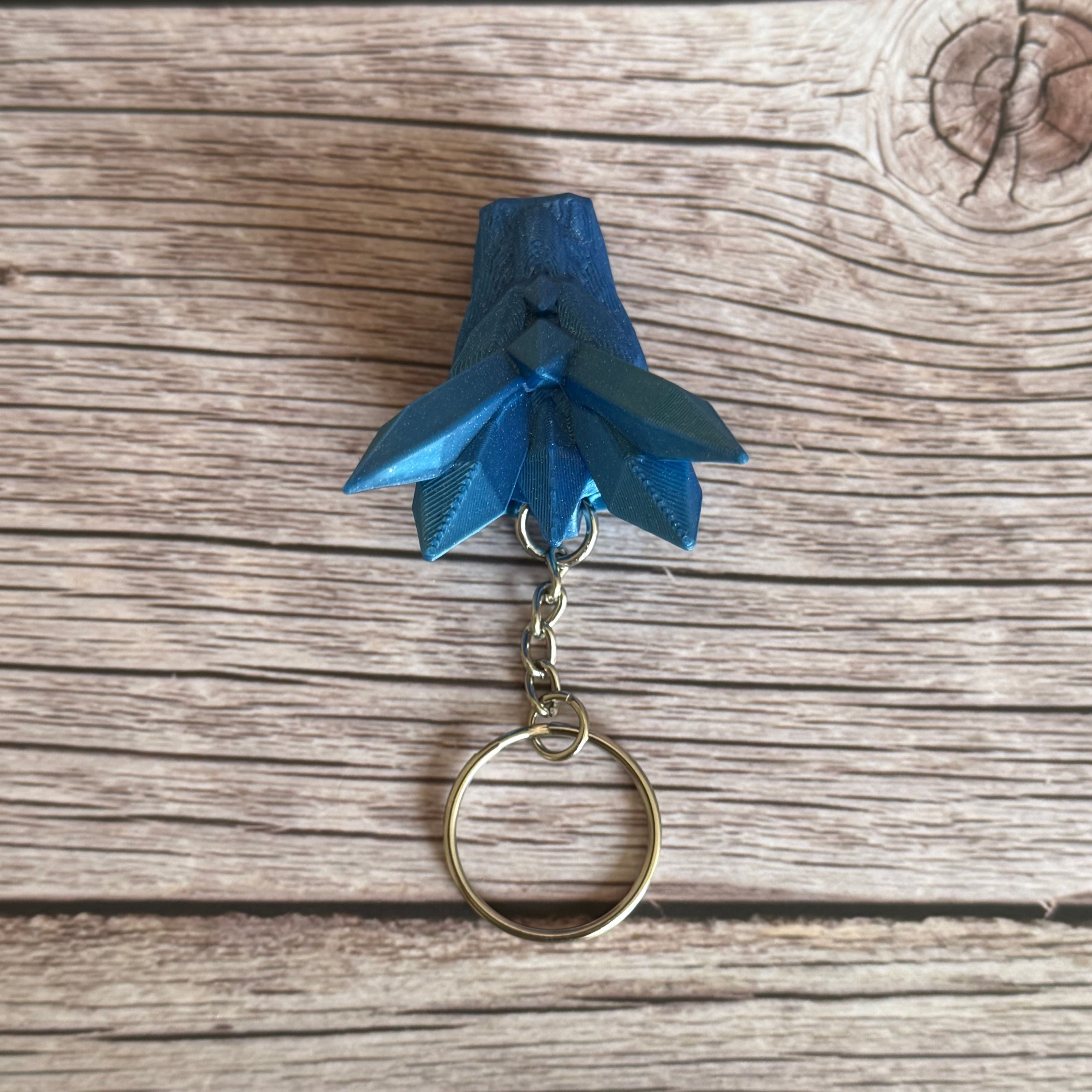 Top of a blue 3D printed keychain shaped like a dragon head with crystal-like details, placed on a wooden surface