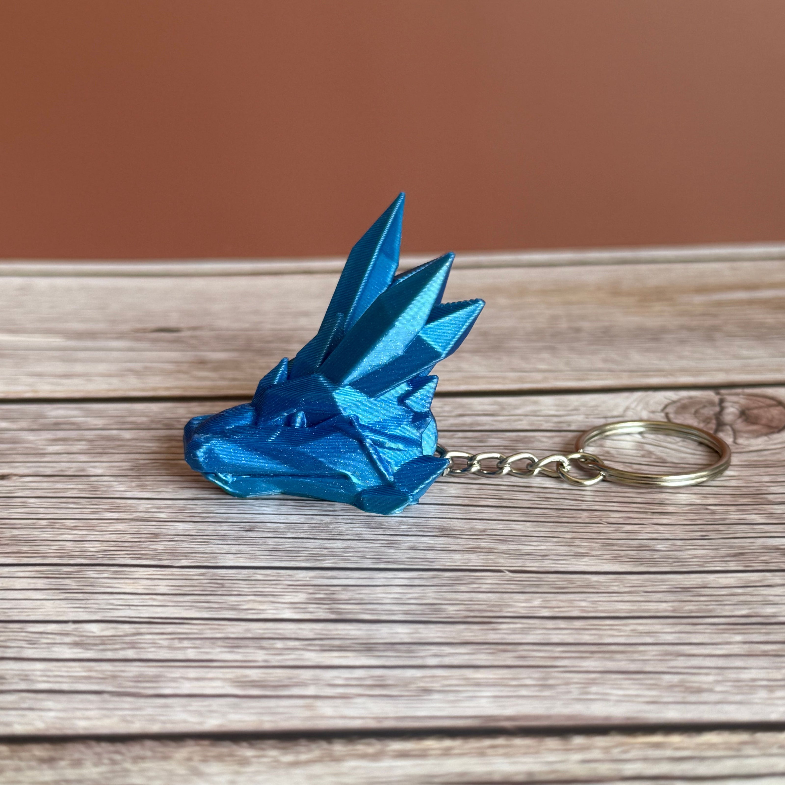 Side of a blue 3D printed keychain shaped like a dragon head with crystal-like details, placed on a wooden surface