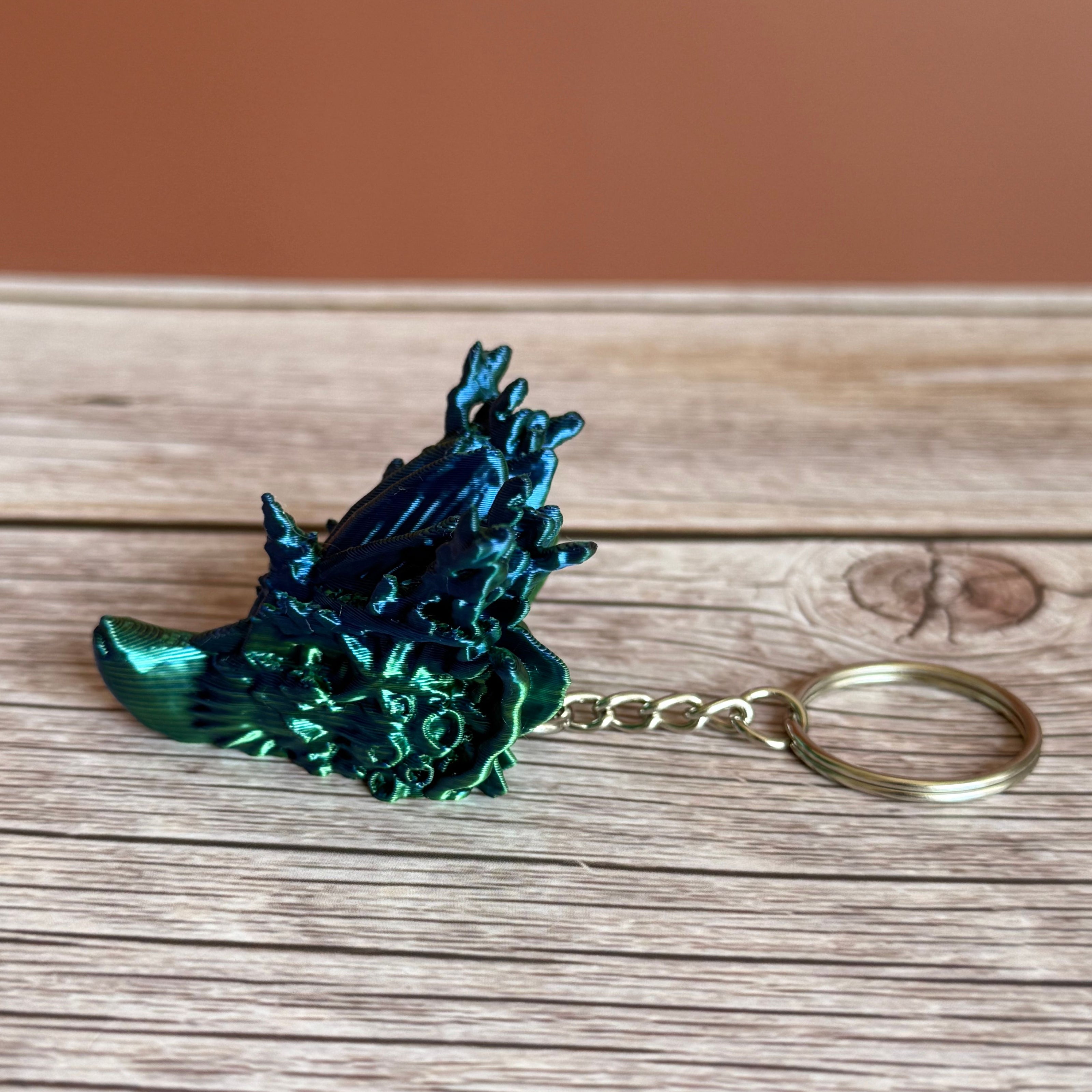 Side of a 3D printed keychain shaped like a dragon head with coral-like details, primarily in green and blue colors, placed on a wooden surface
