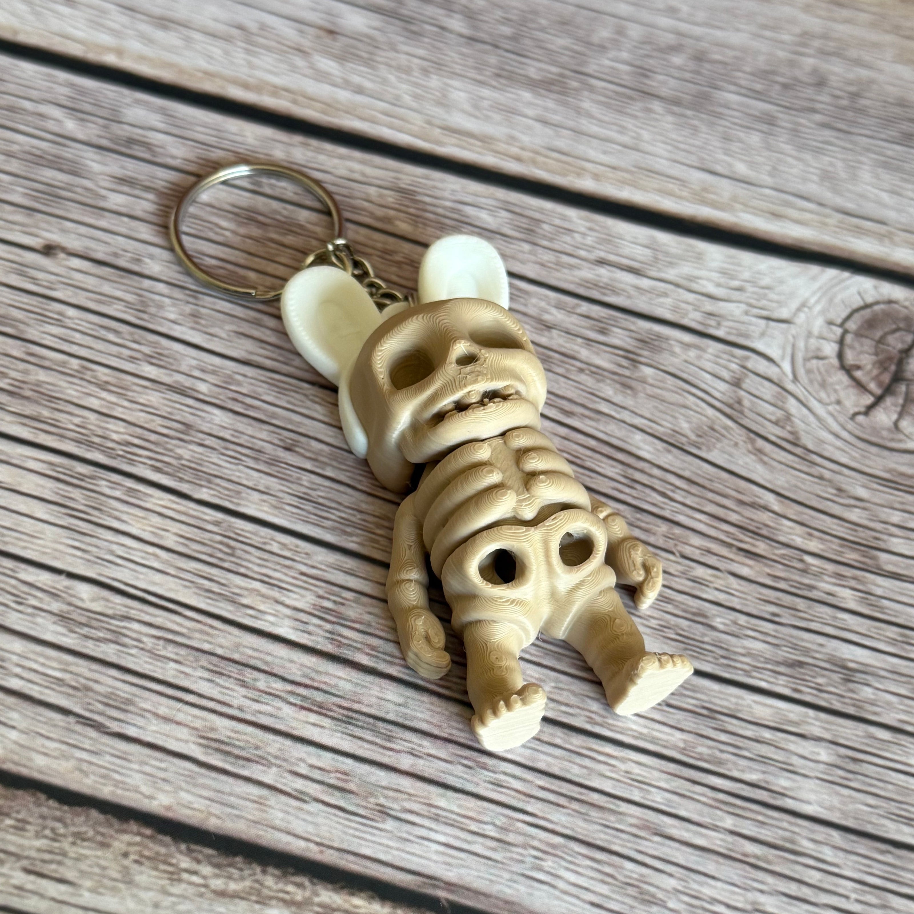 3D printed keychain of a beige skeleton with white bunny ears on a wooden surface