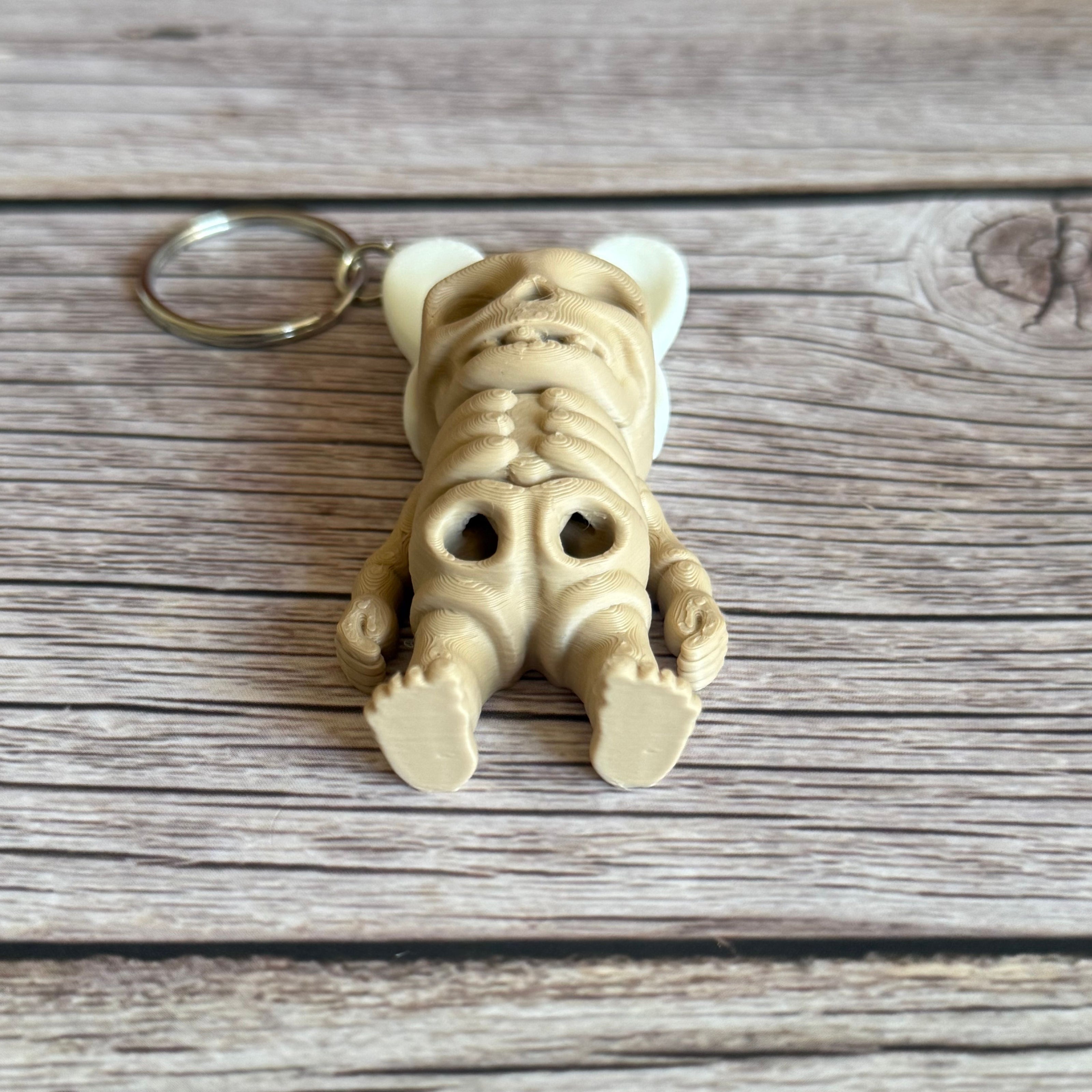 3D printed keychain of a beige skeleton with white bunny ears on a wooden surface