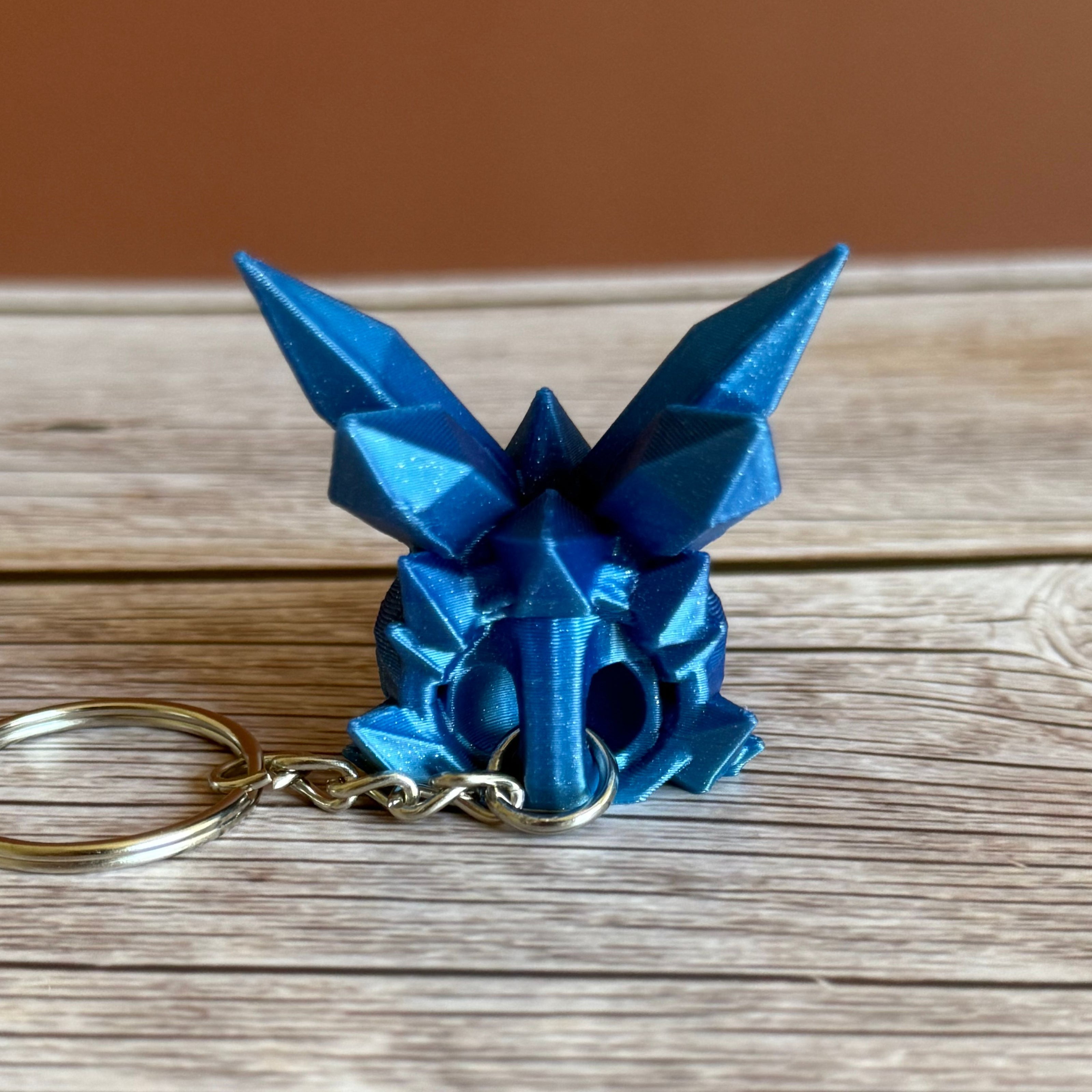 Back of a blue 3D printed keychain shaped like a dragon head with crystal-like details, placed on a wooden surface