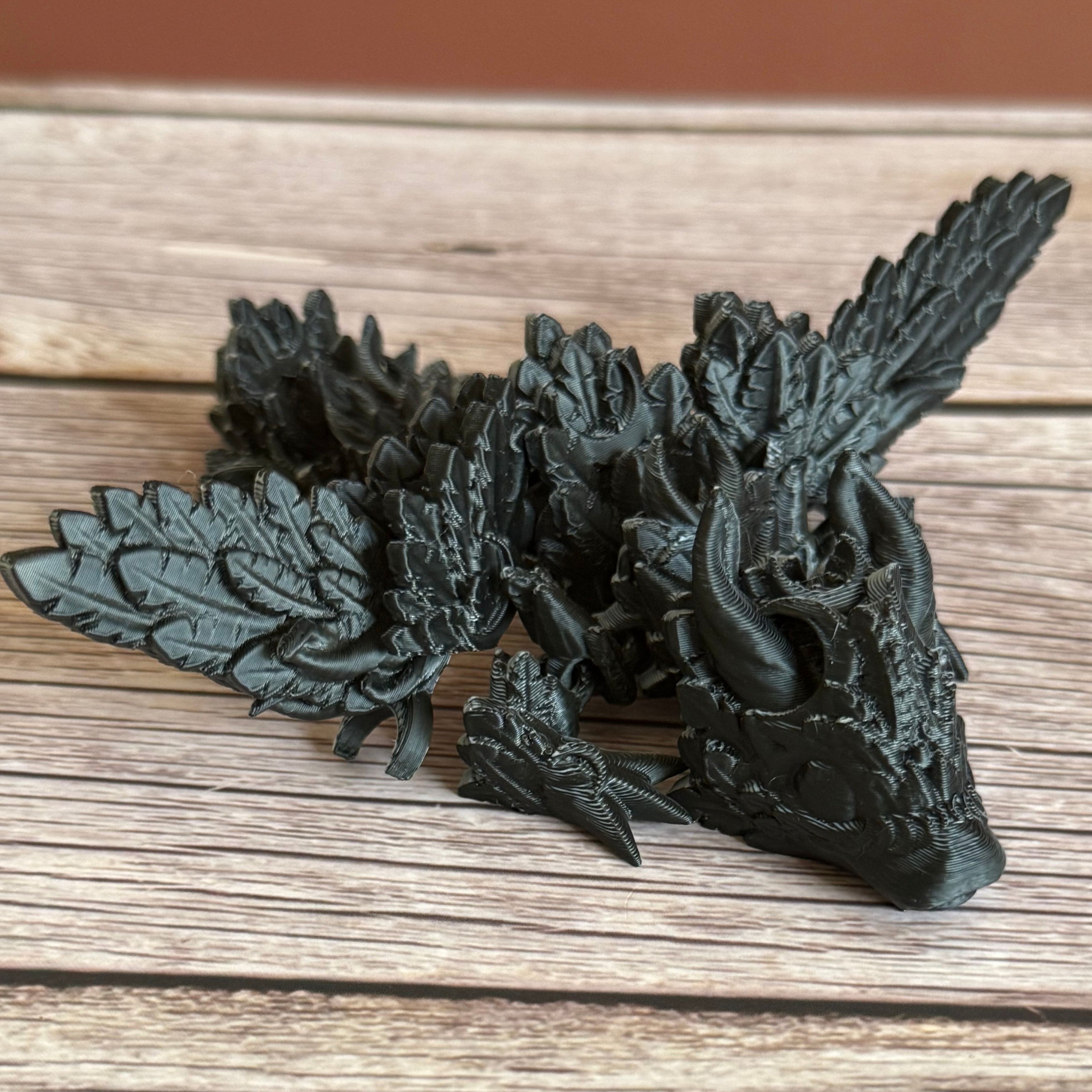 A 3D printed, articulated dragon toy with black and white celestial-inspired patterns on a wooden surface.
