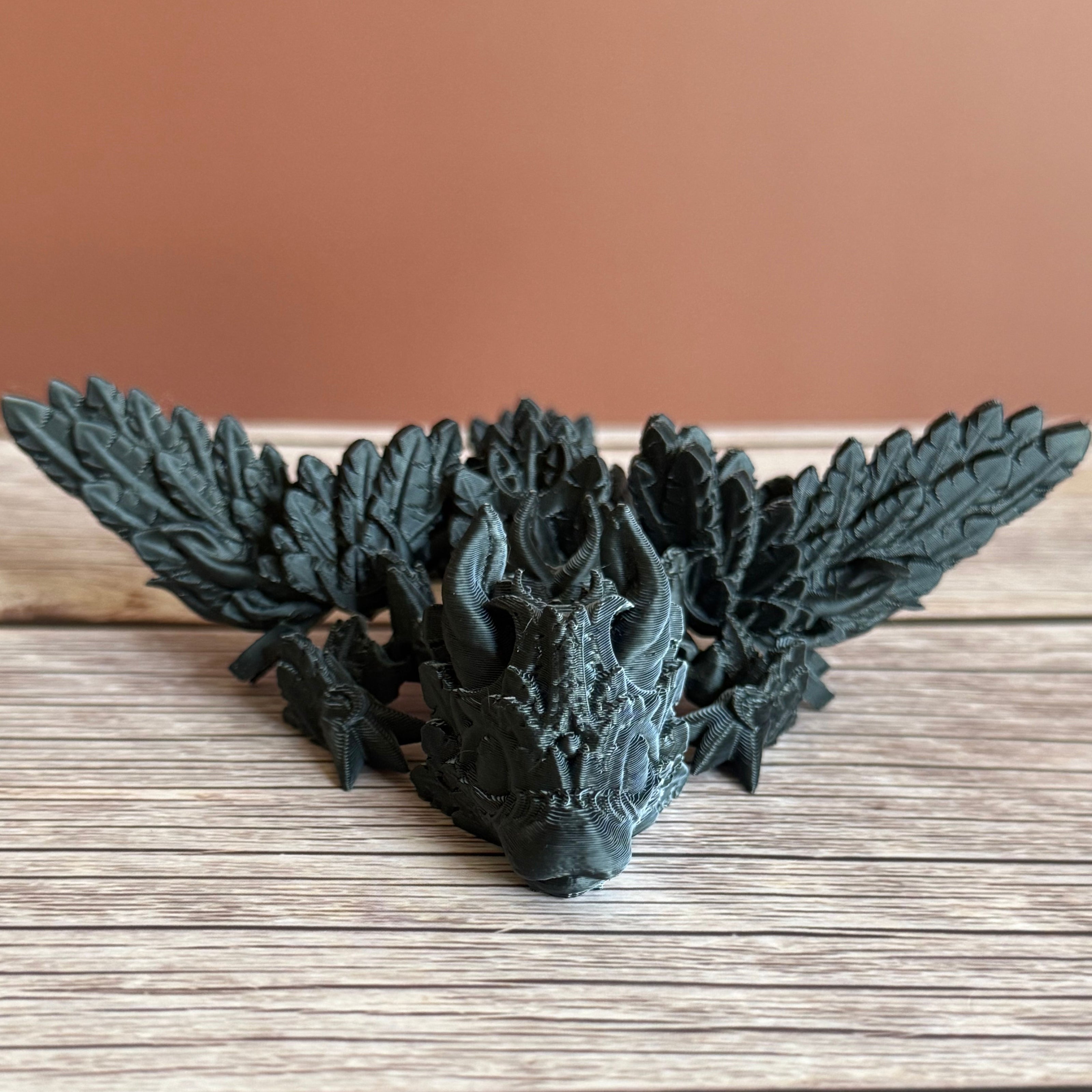 A 3D printed, articulated dragon toy with black and white celestial-inspired patterns on a wooden surface.