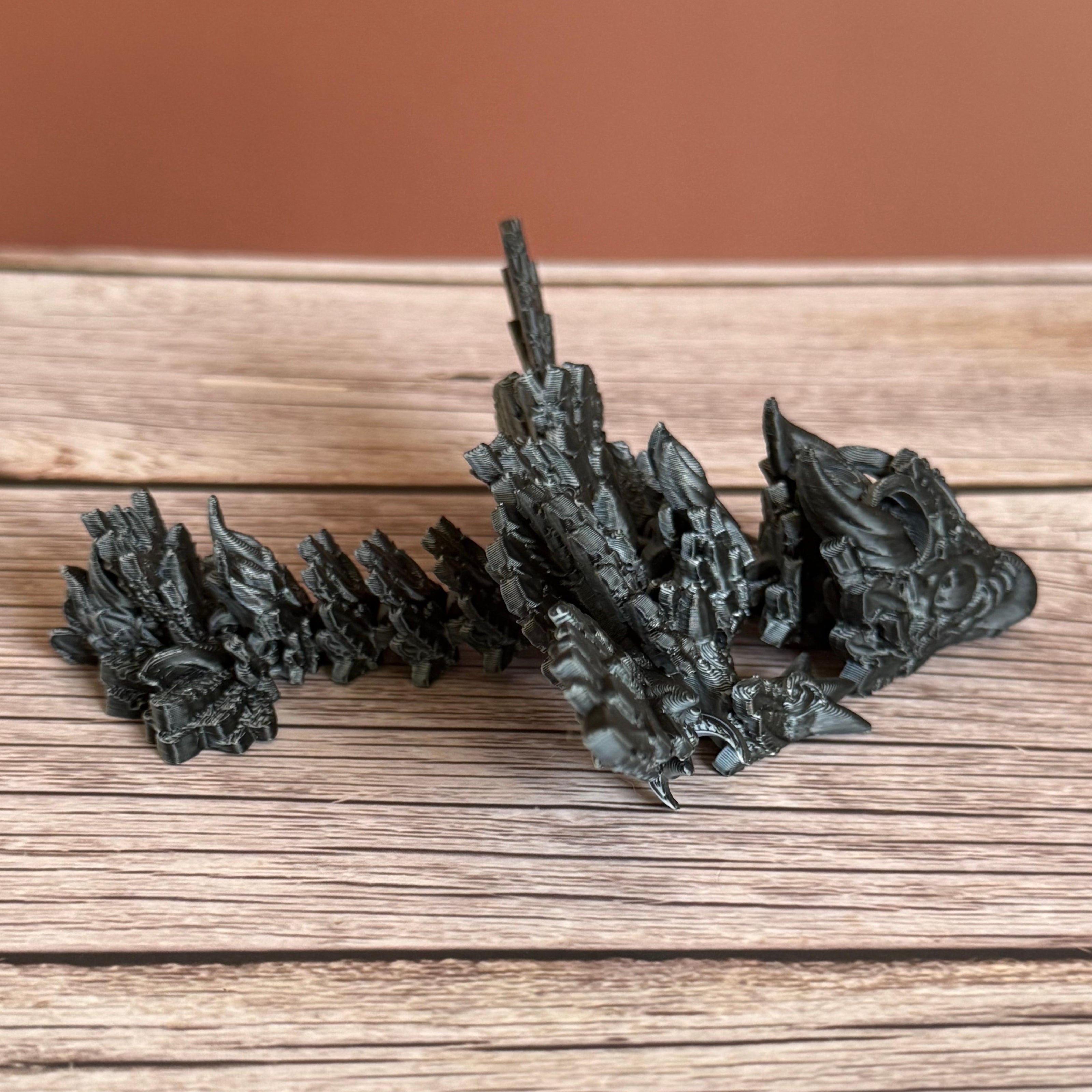A 3D printed, articulated dragon toy with black and white celestial-inspired patterns on a wooden surface.