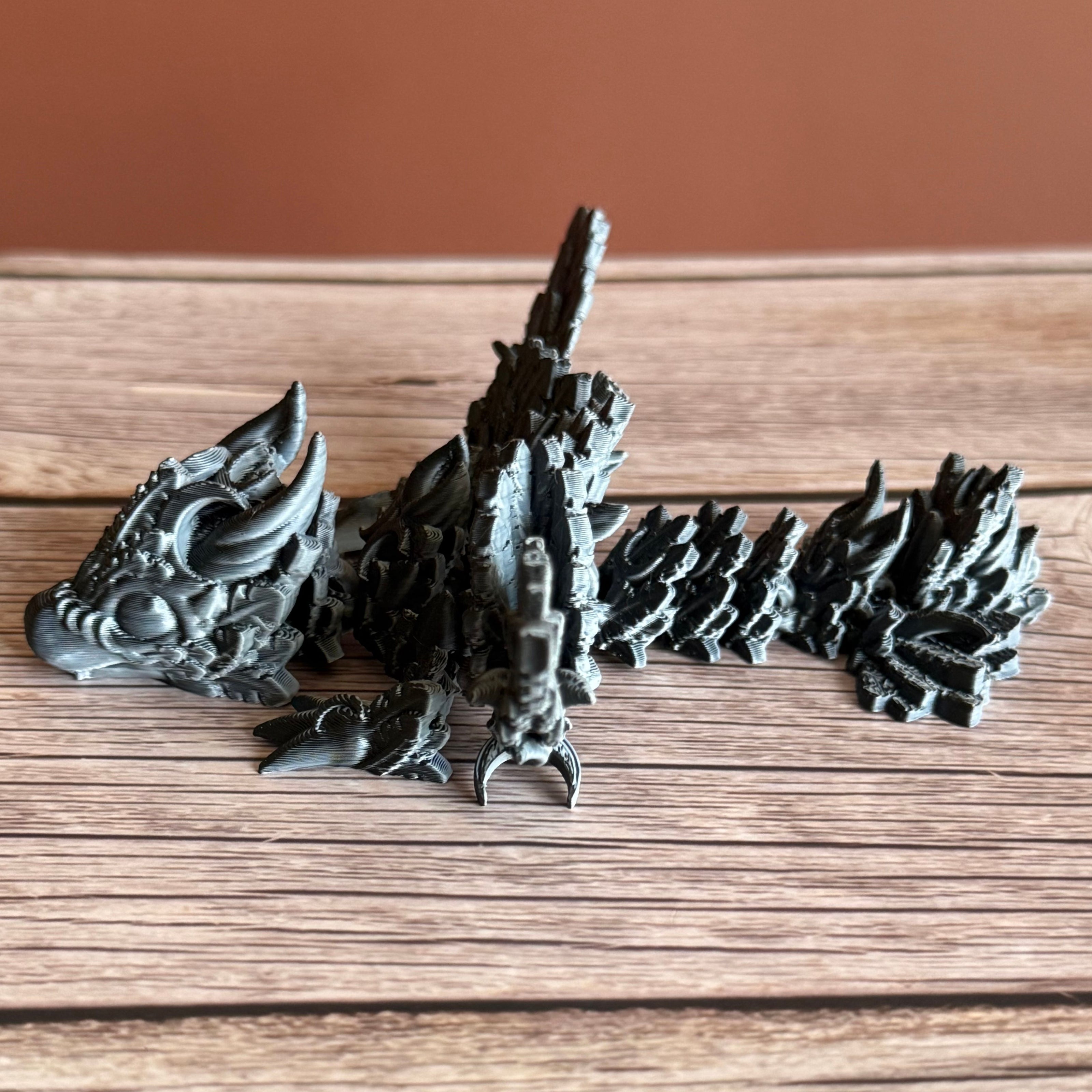 A 3D printed, articulated dragon toy with black and white celestial-inspired patterns on a wooden surface.