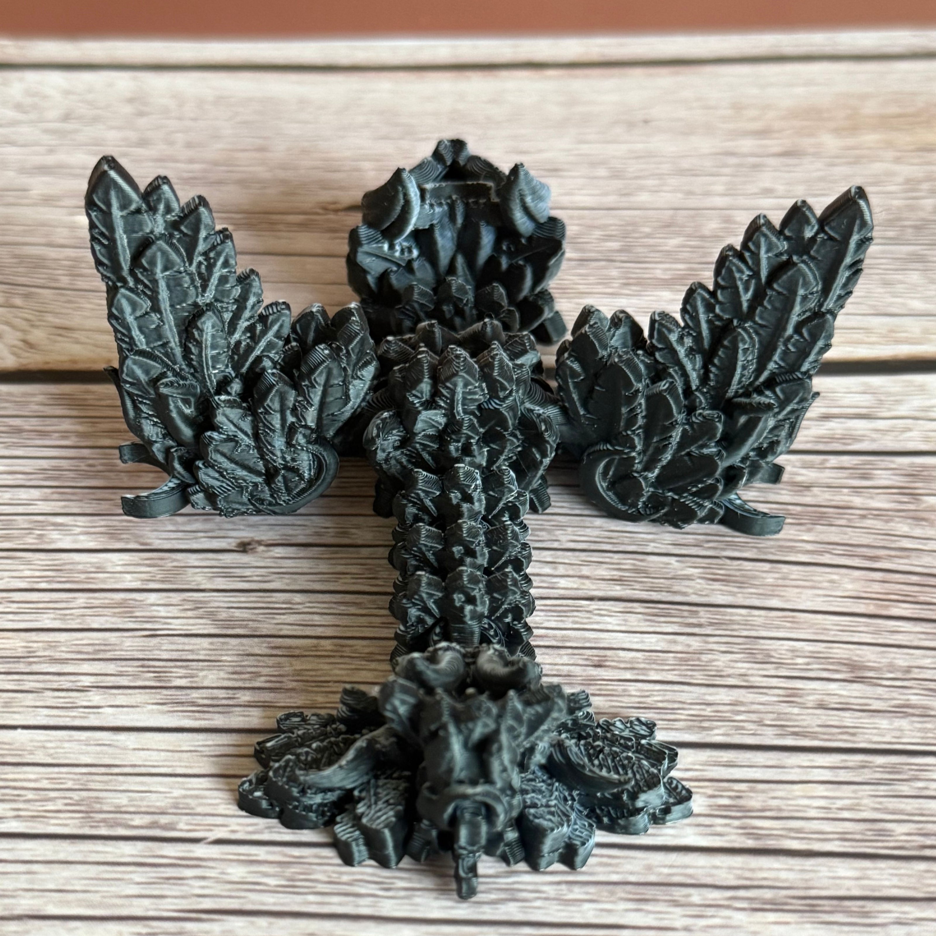 A 3D printed, articulated dragon toy with black and white celestial-inspired patterns on a wooden surface.