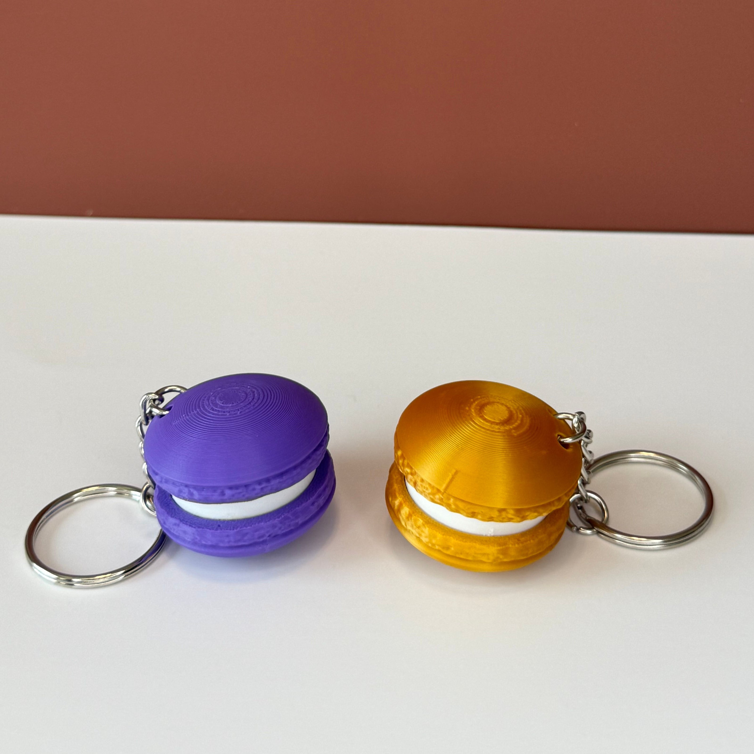 Purple and gold 3D printed macaron-shaped keychains on a white surface with a brown backdrop