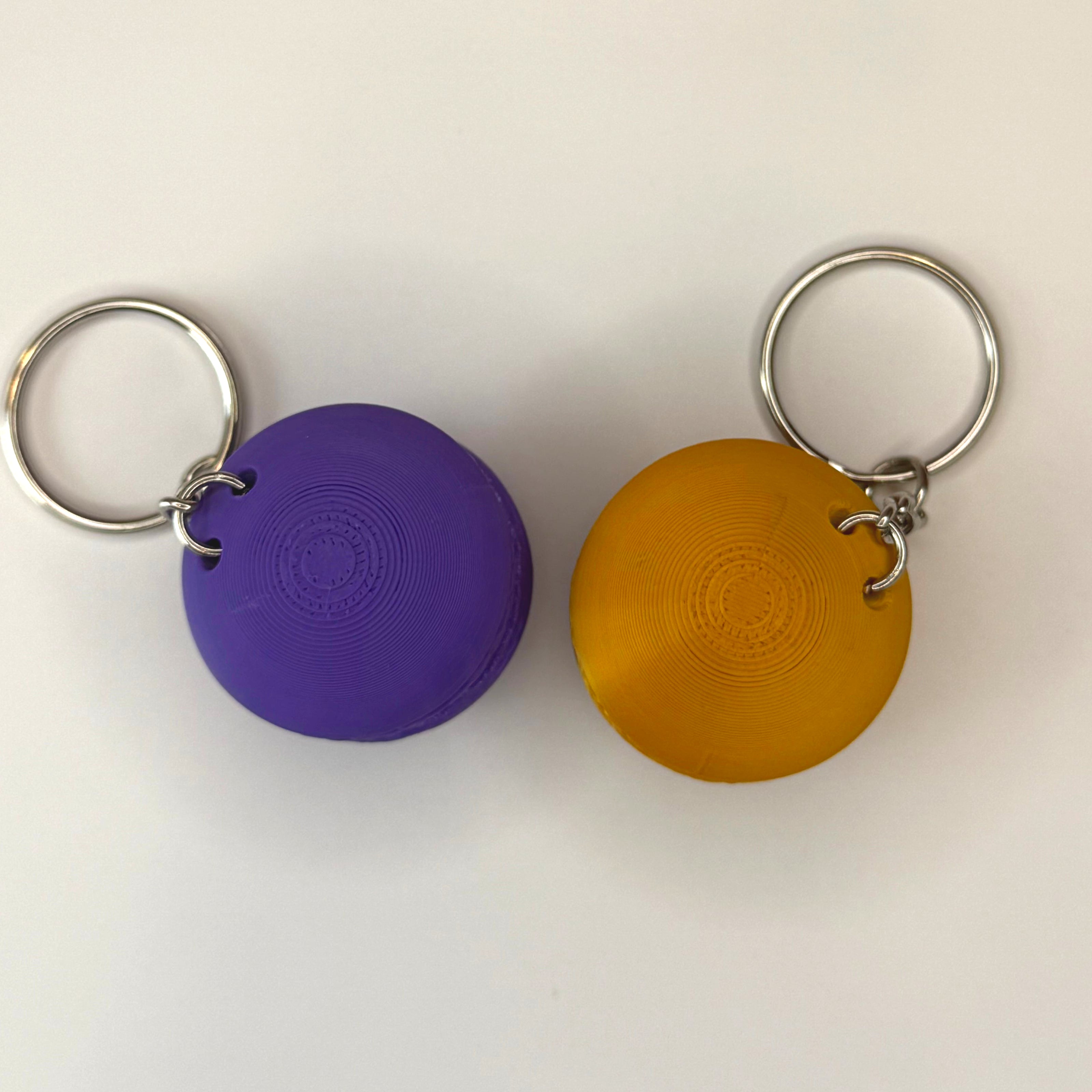 Tops of purple and gold 3D printed macaron-shaped keychains on a white surface 