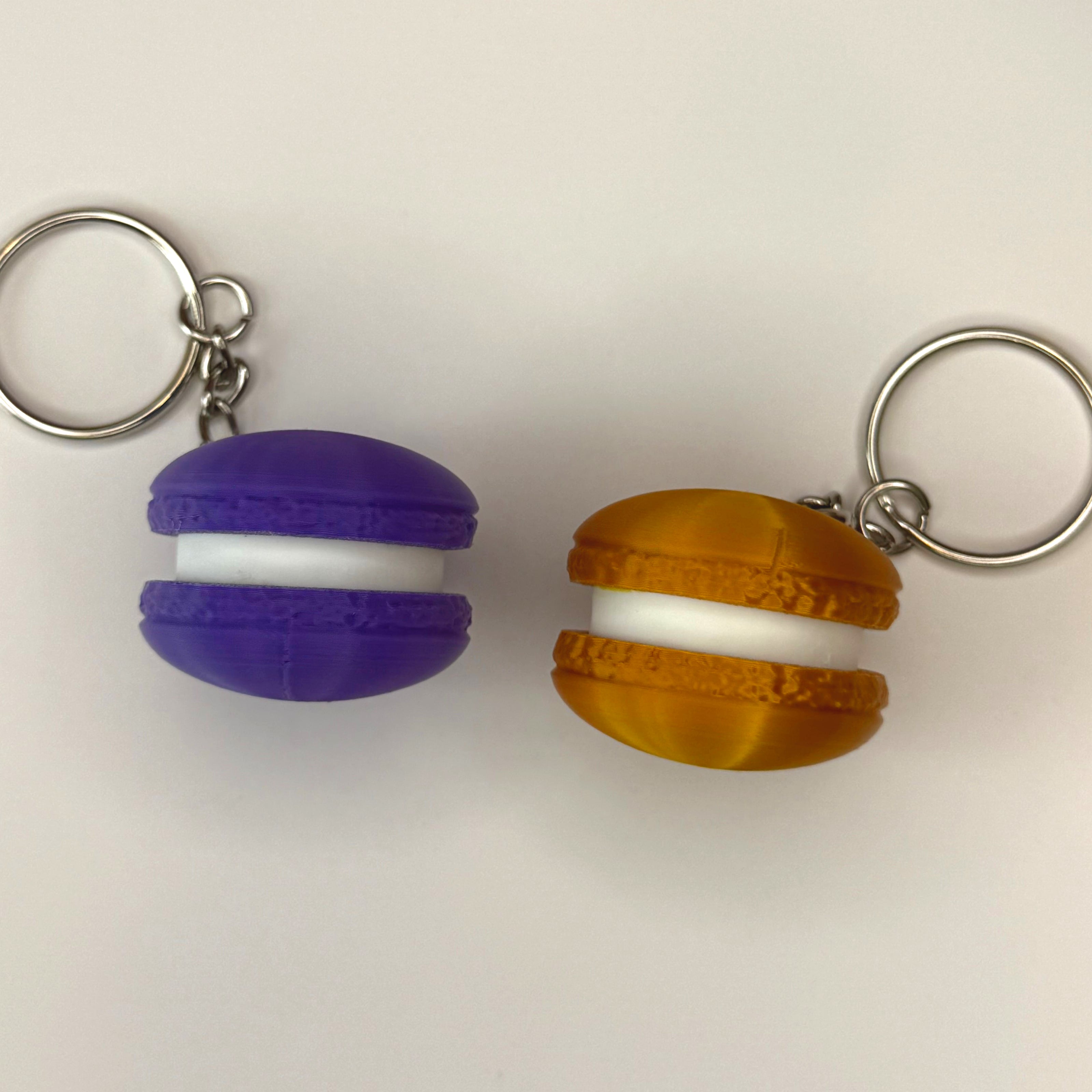Purple and gold 3D printed macaron-shaped keychains on a white surface 