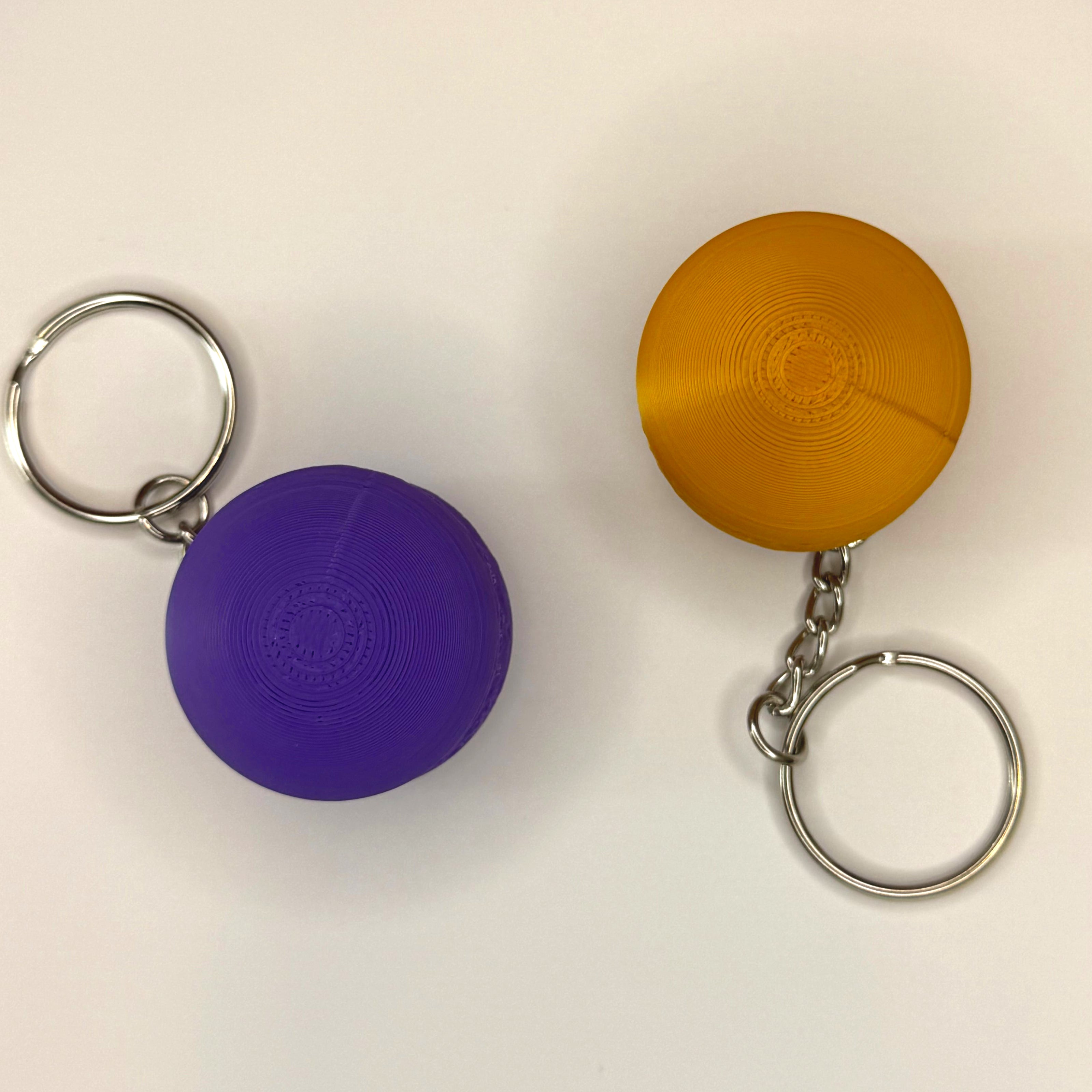 Tops of purple and gold 3D printed macaron-shaped keychains on a white surface