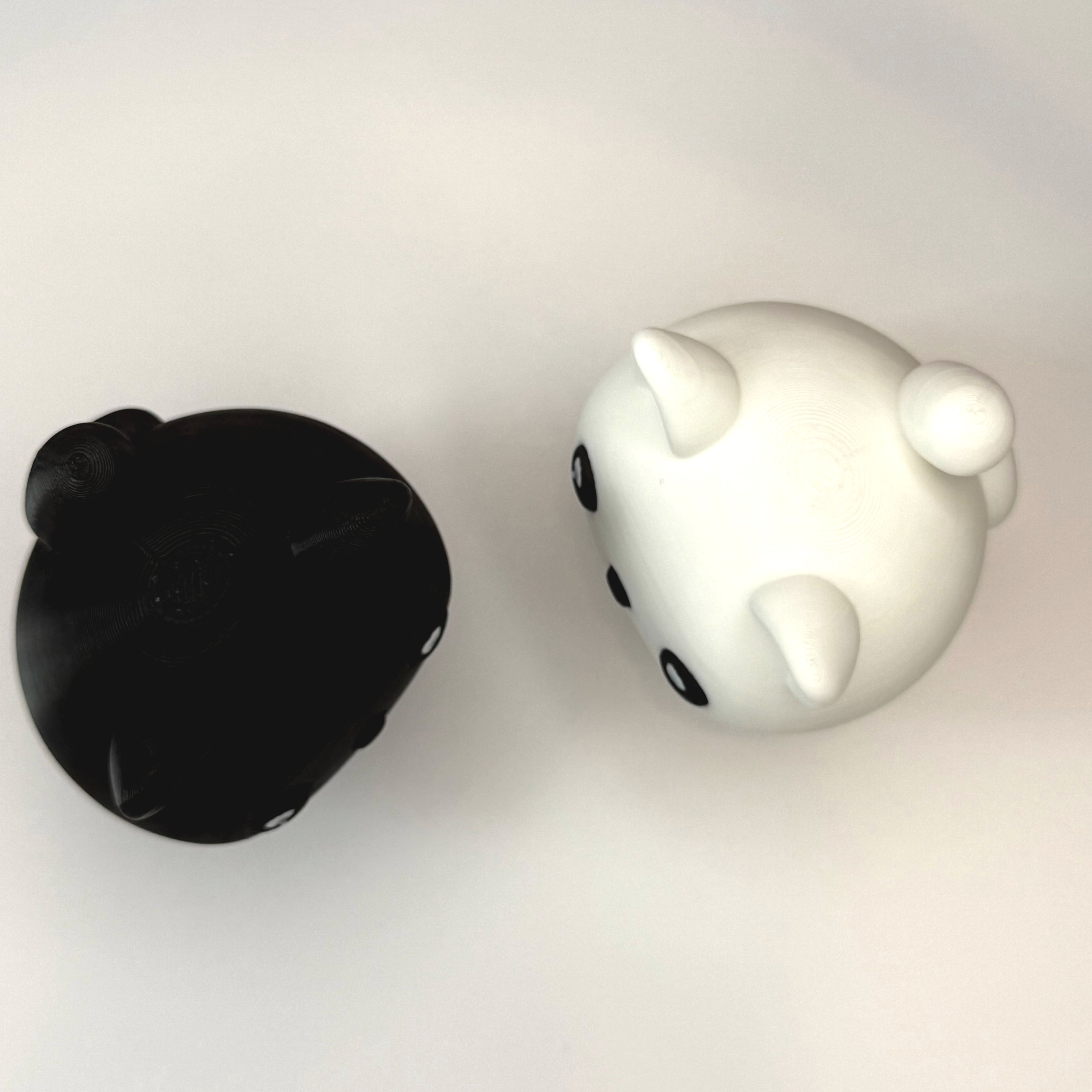 Top side of 2 cat-shaped 3D printed figures, one black and one white, on a white surfac