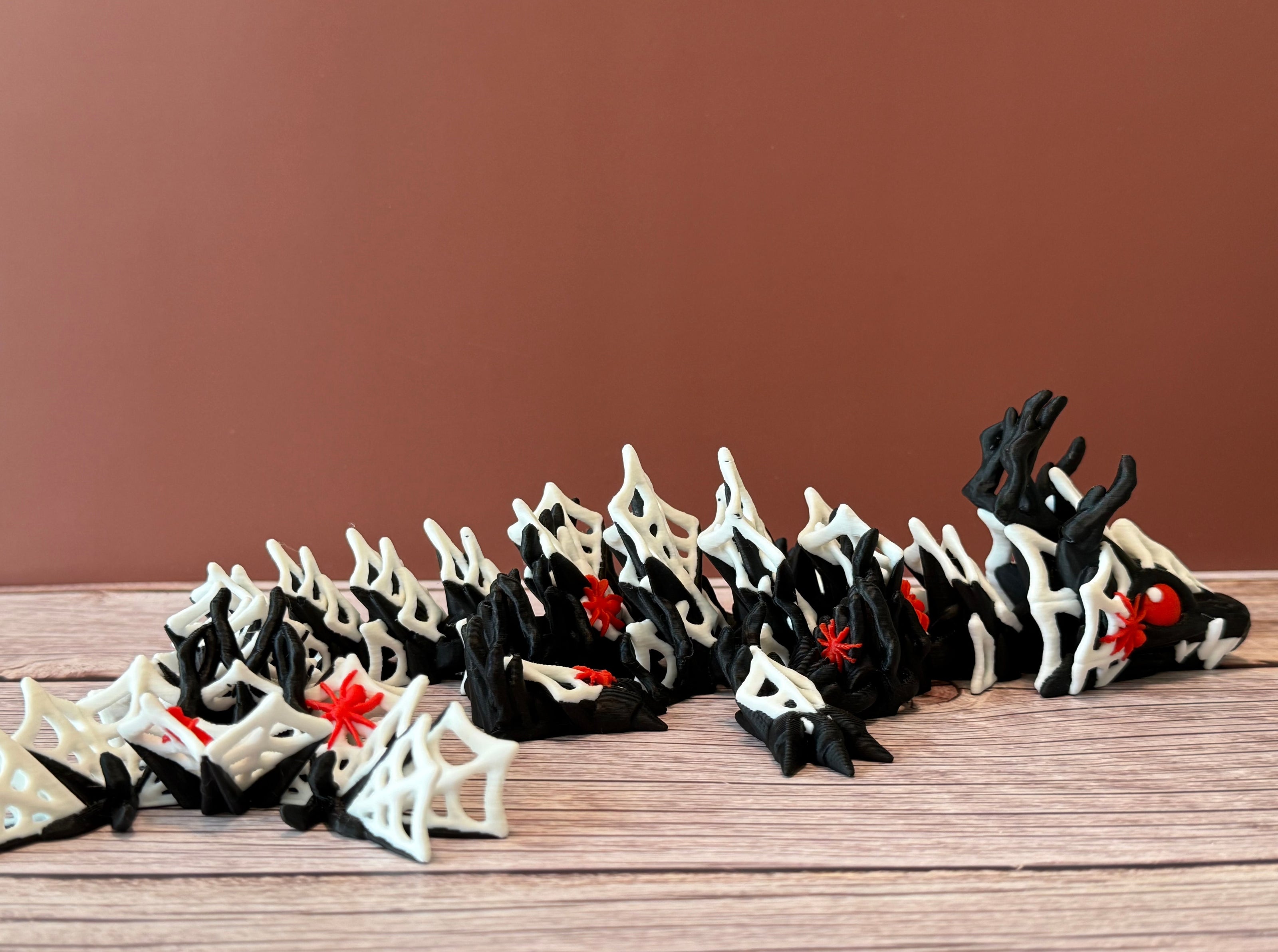 3D printed black dragon with white spider webs and red spiders across the body, placed on a wooden surface with a brown backdrop