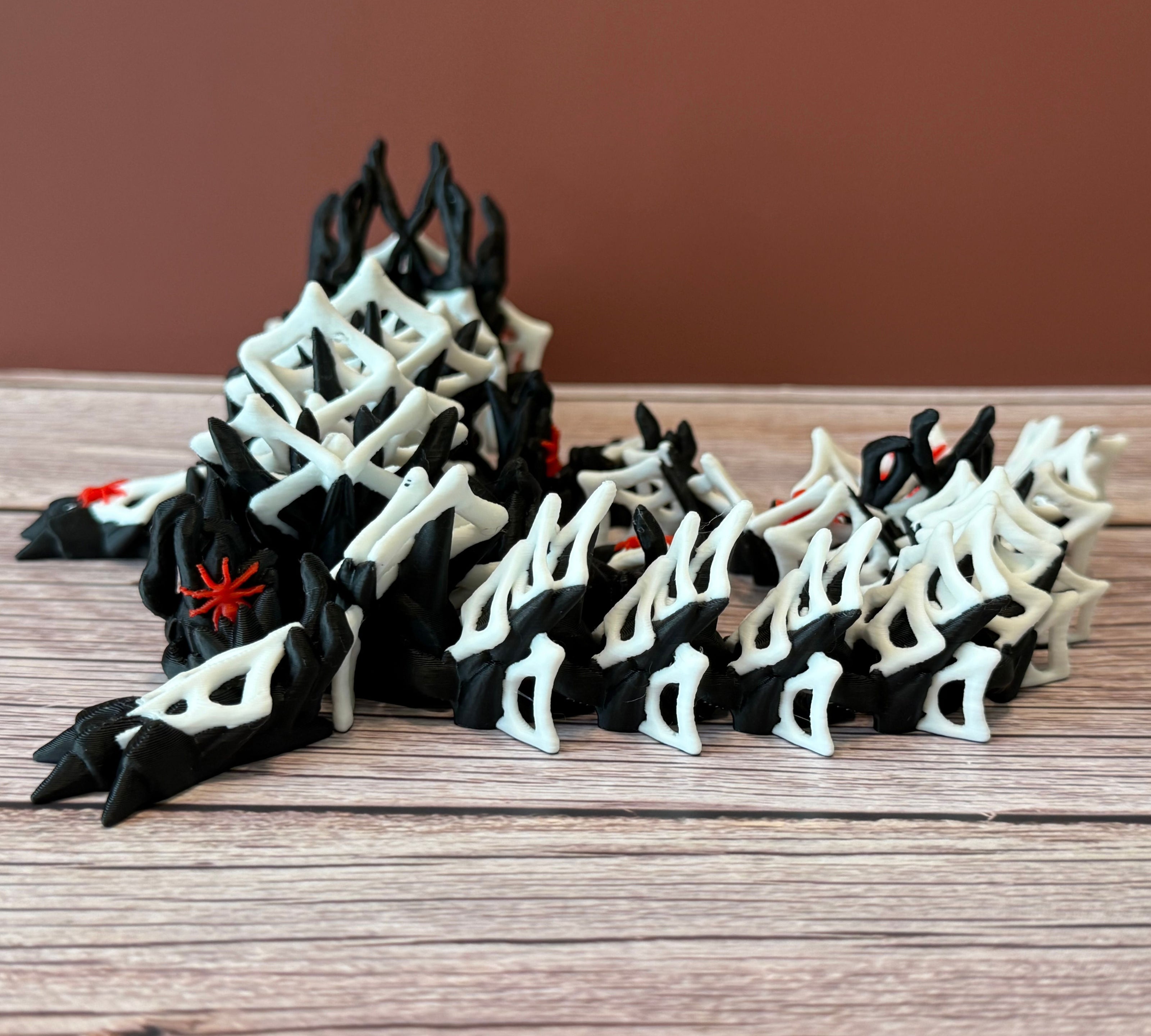 3D printed black dragon with white spider webs and red spiders across the body, placed on a wooden surface with a brown backdrop