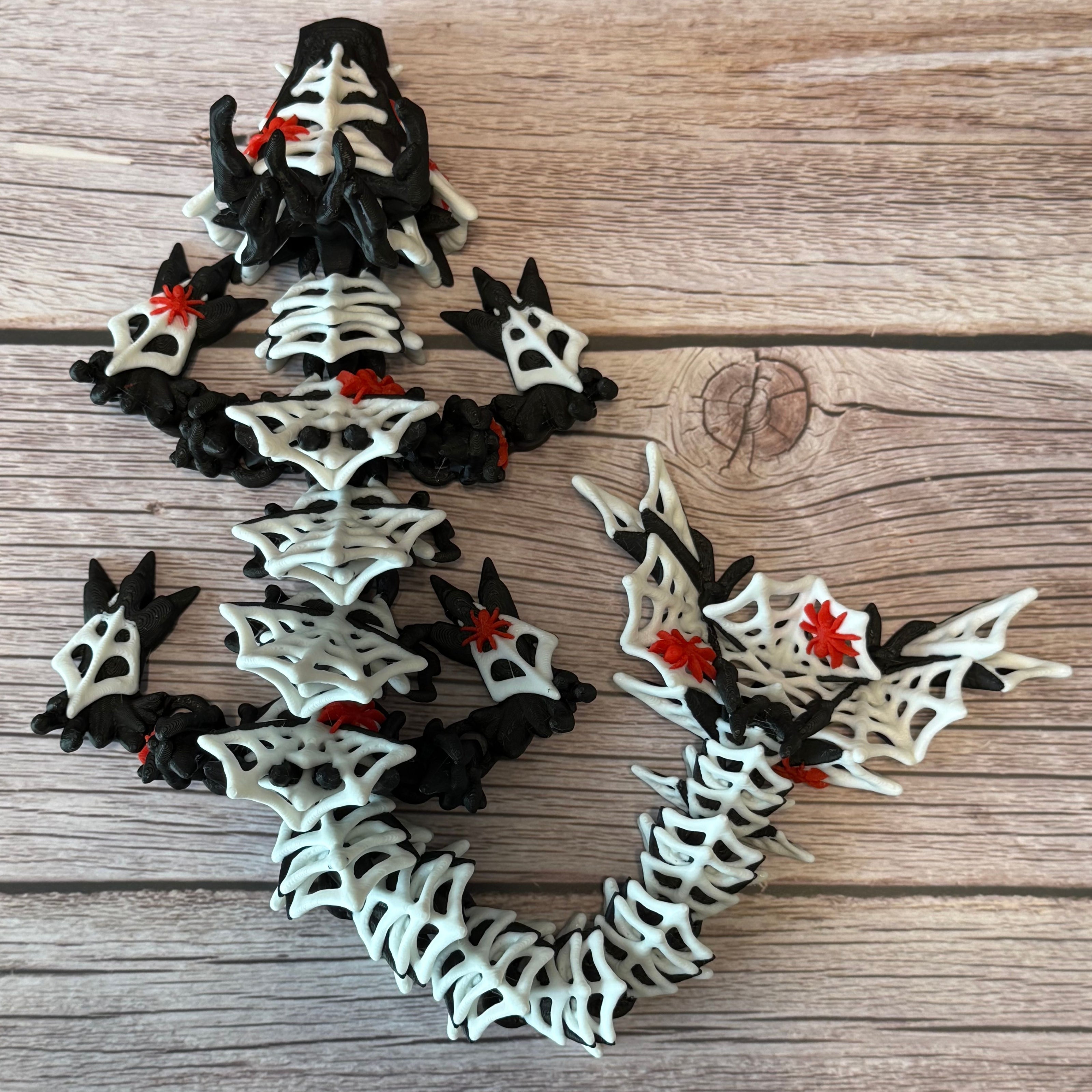 3D printed black dragon with white spider webs and red spiders across the body, placed on a wooden surface with a brown backdrop