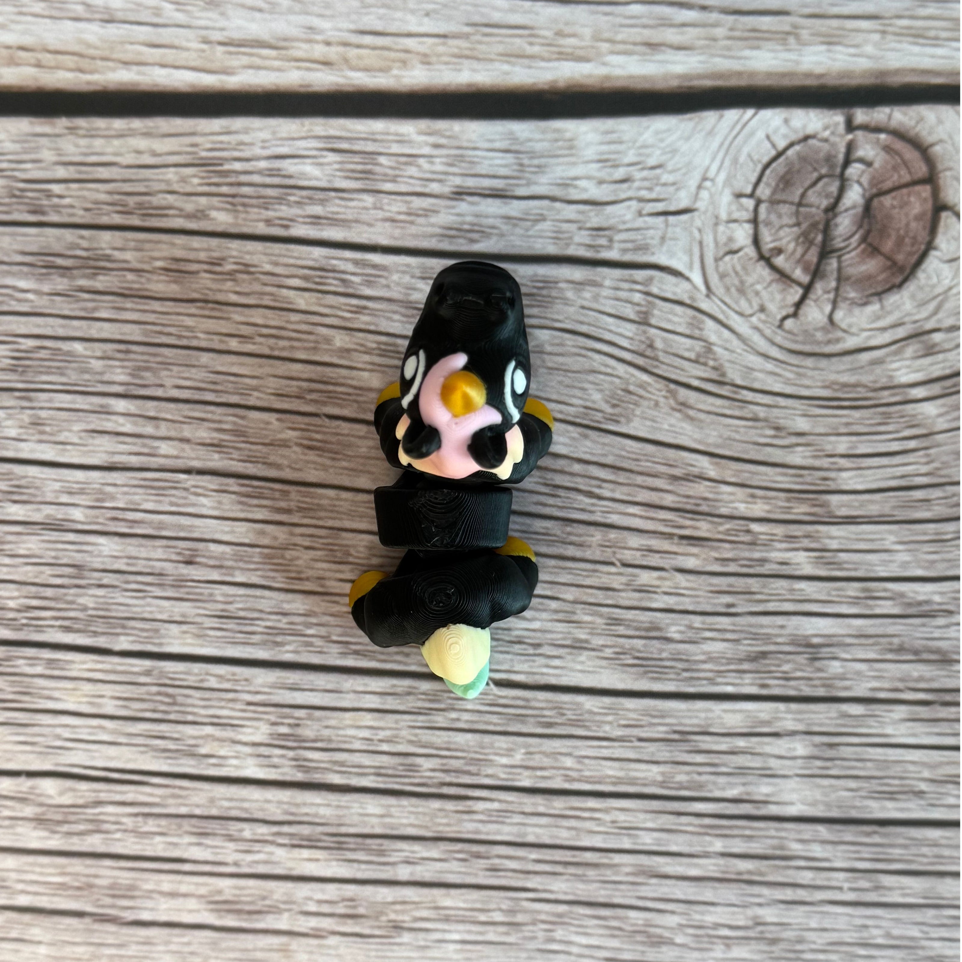A small 3D printed articulated mini unicorn toy with articulated segments, black body, rainbow hair, and golden hooves and horn on a wooden surface