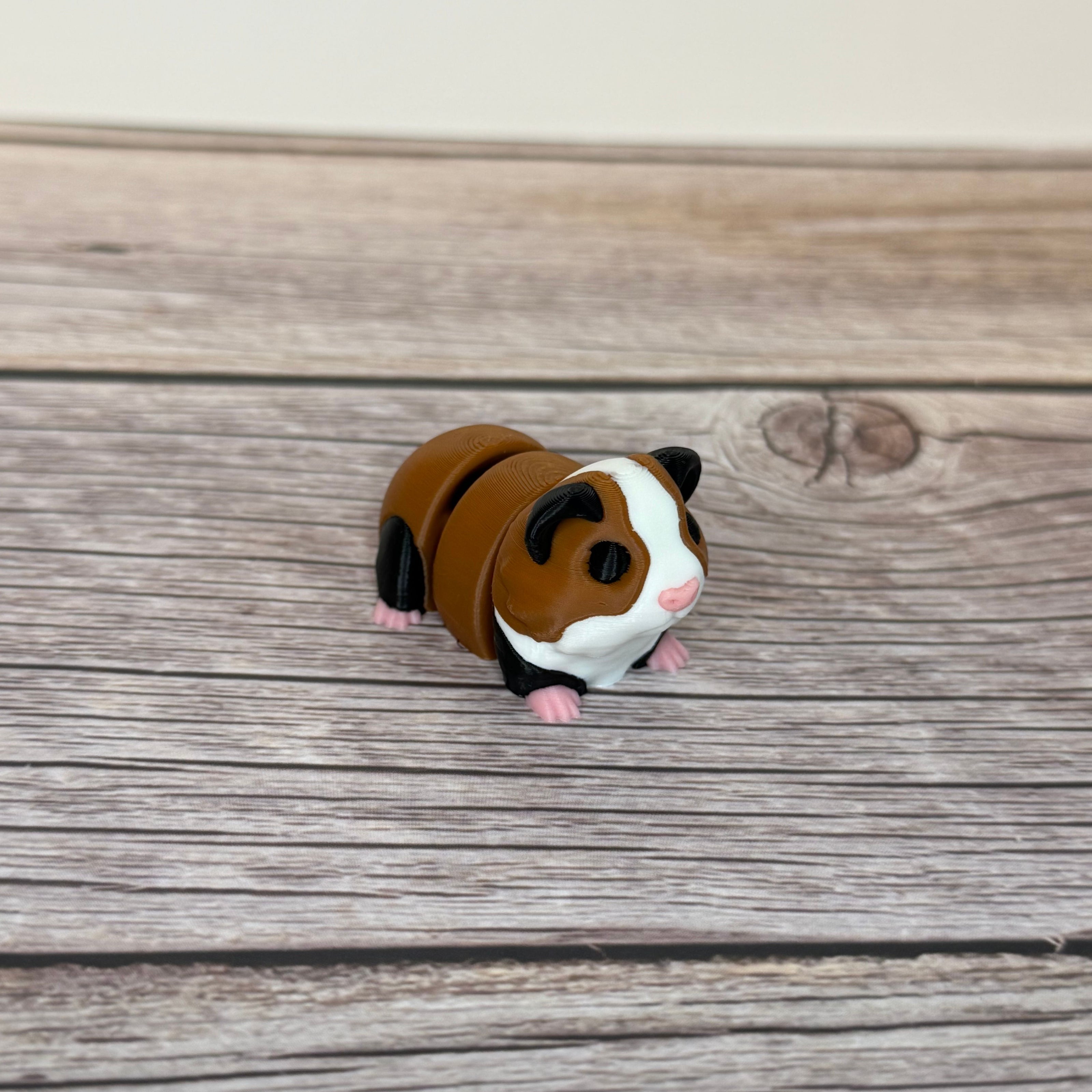 A small 3D printed articulated mini guinea pig toy with articulated segments, placed on a wooden surface.