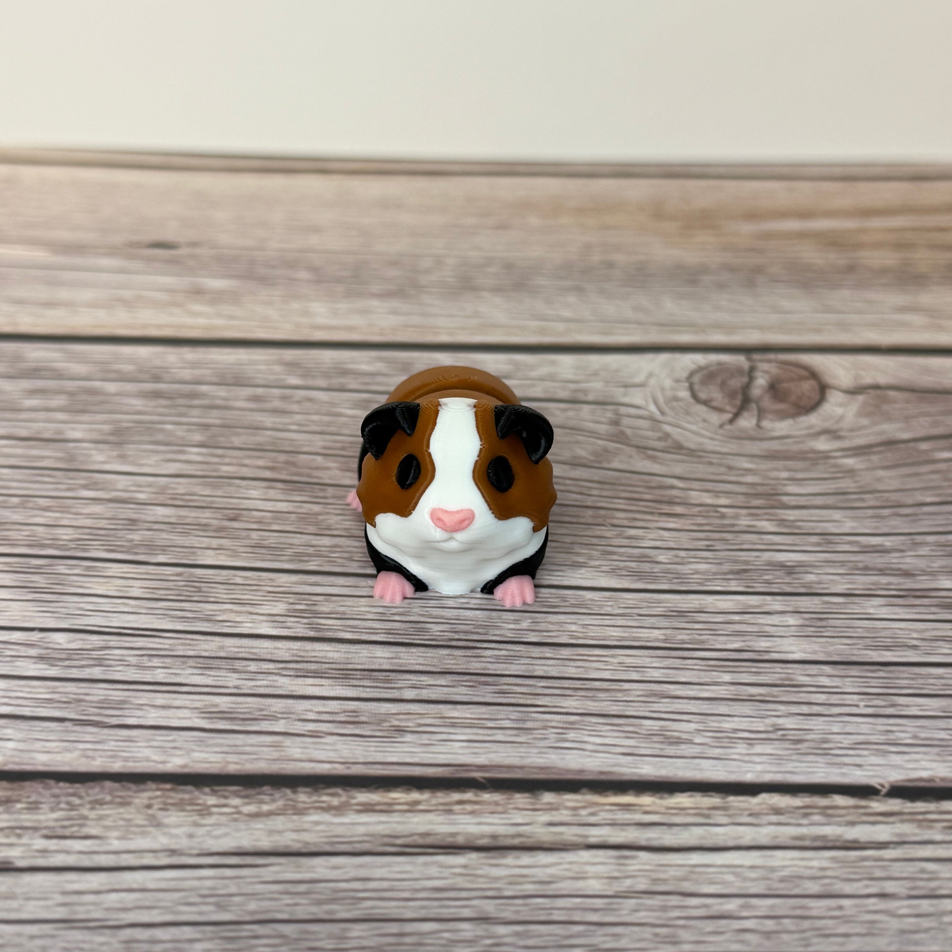 A small 3D printed articulated mini guinea pig toy with articulated segments, placed on a wooden surface.