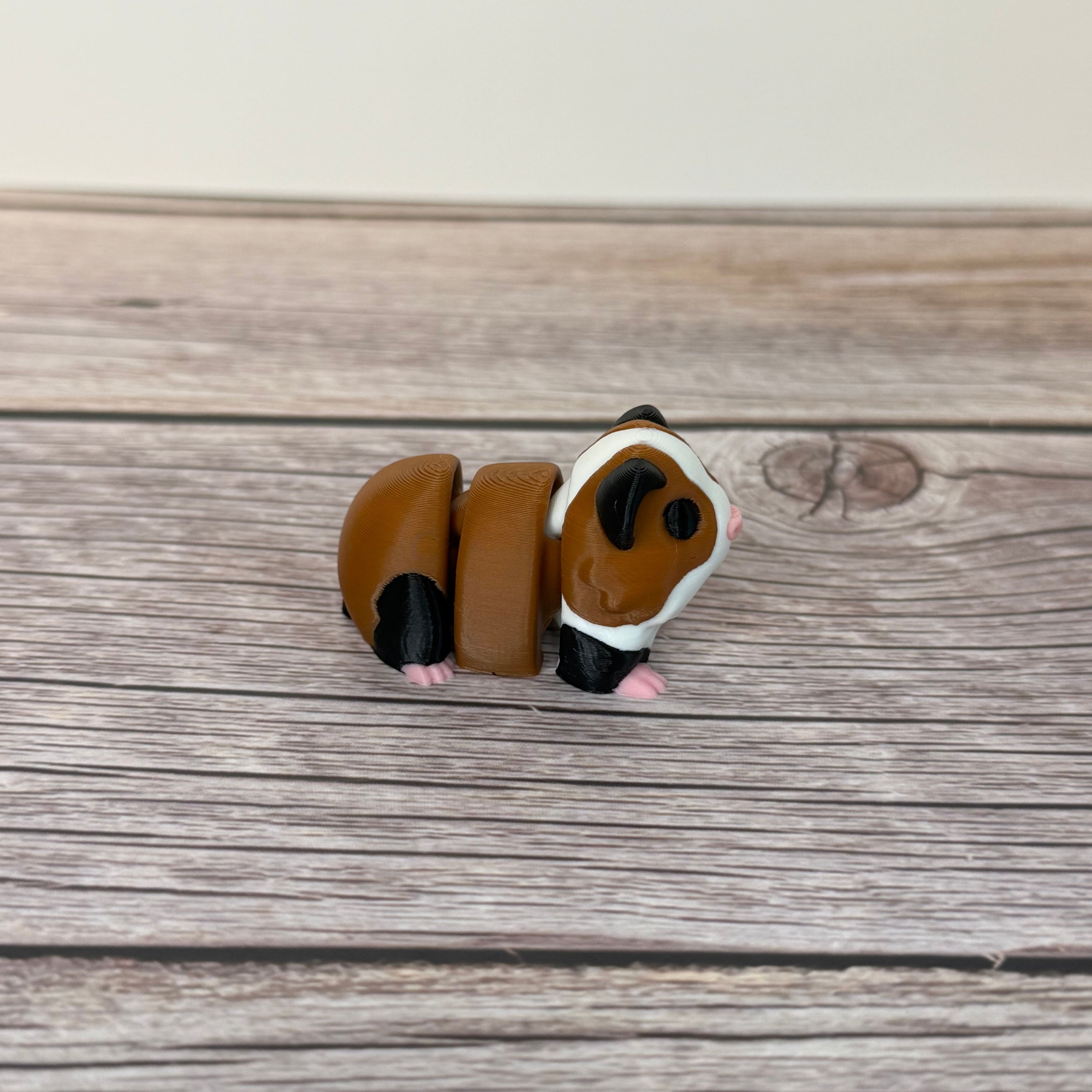 A small 3D printed articulated mini guinea pig toy with articulated segments, placed on a wooden surface.