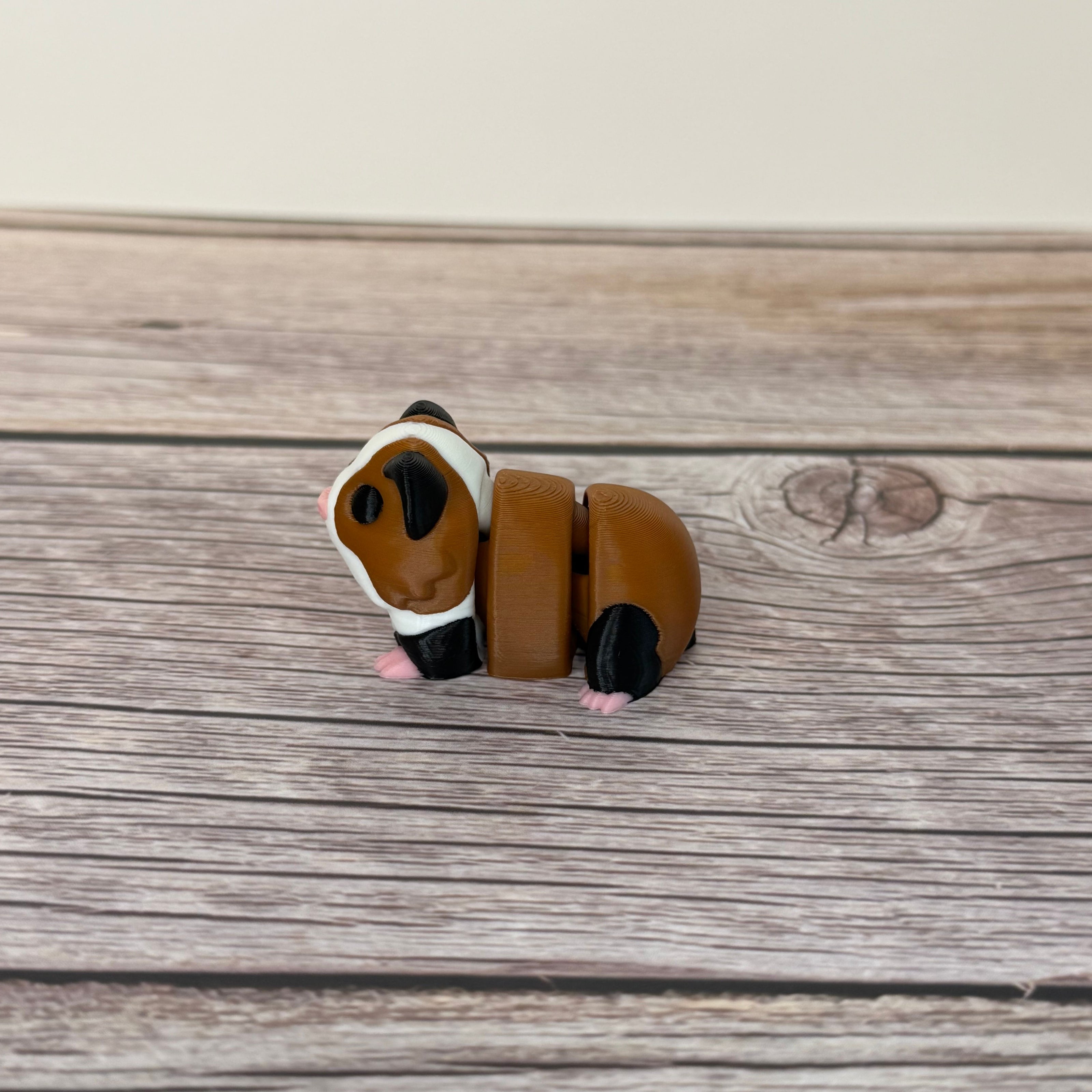 A small 3D printed articulated mini guinea pig toy with articulated segments, placed on a wooden surface.