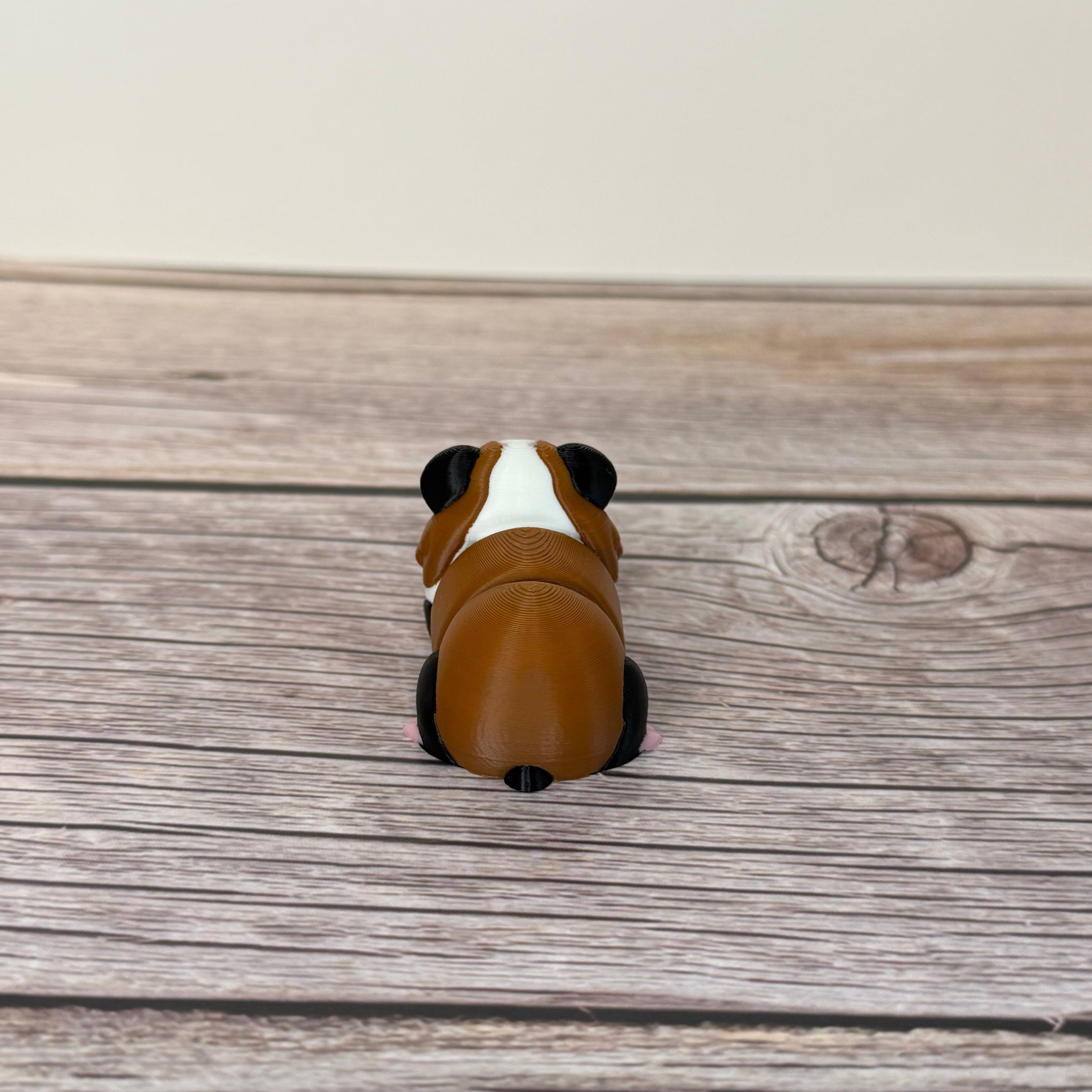 A small 3D printed articulated mini guinea pig toy with articulated segments, placed on a wooden surface.