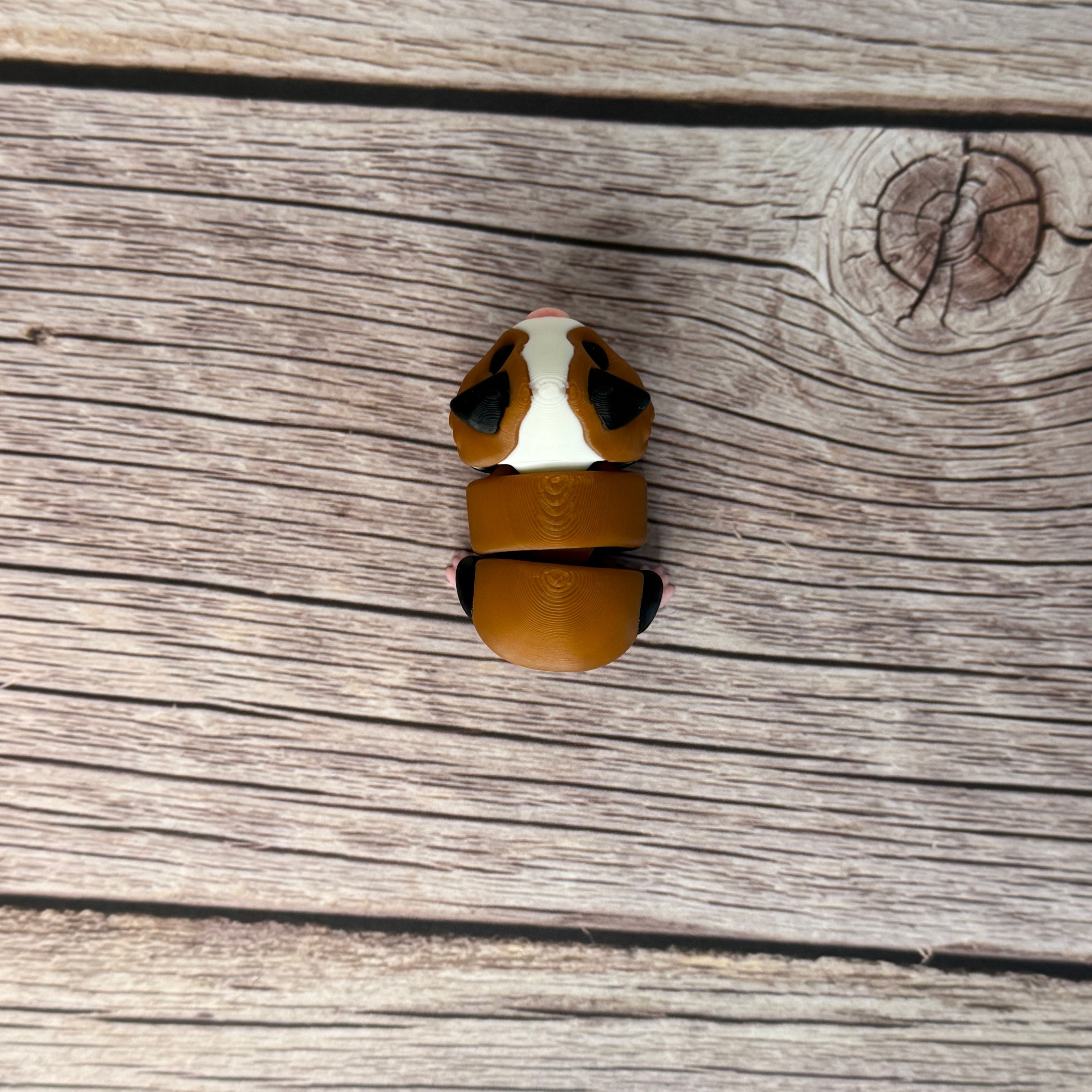 A small 3D printed articulated mini guinea pig toy with articulated segments, placed on a wooden surface.