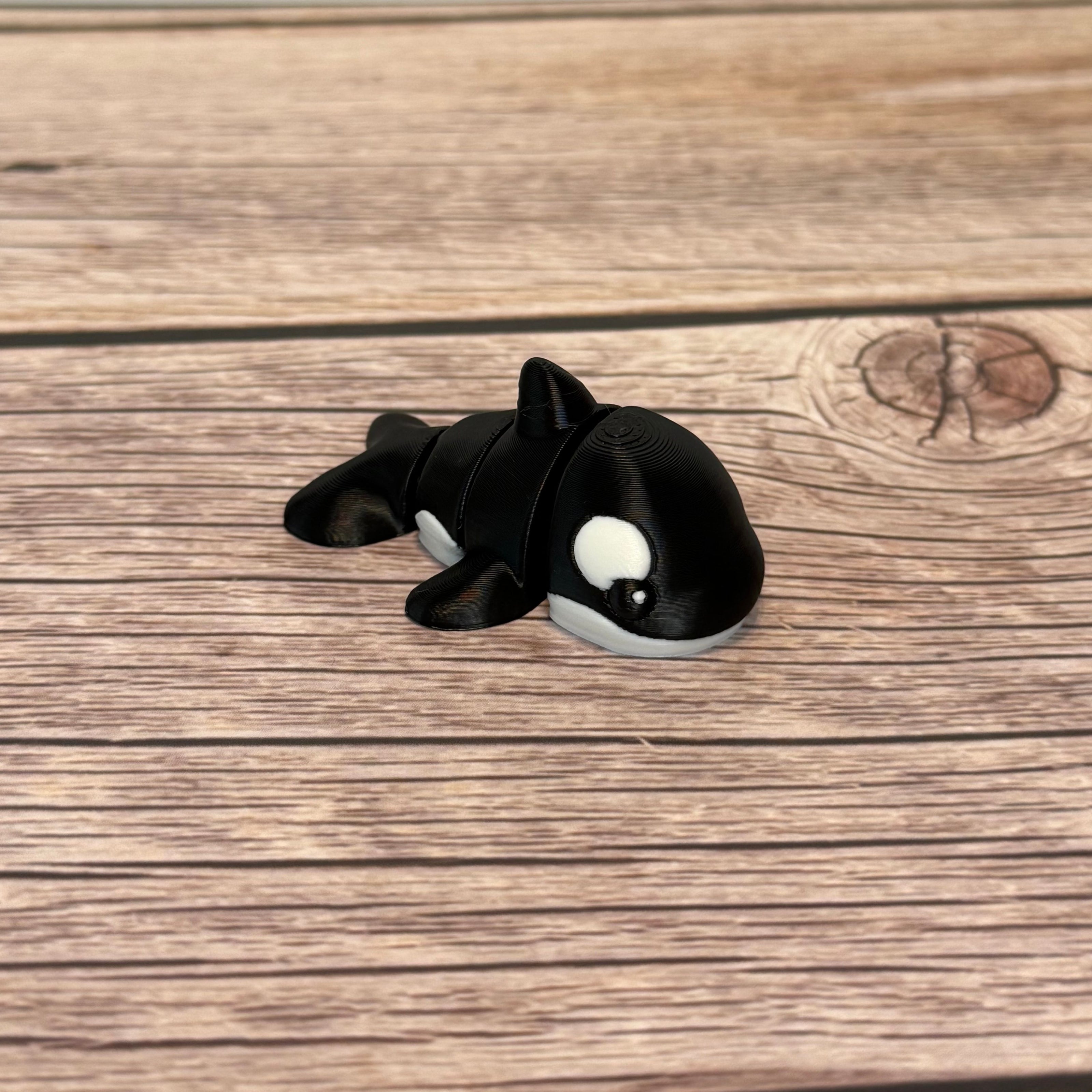 A small 3D printed black and white articulated mini orca toy placed on a wooden surface.