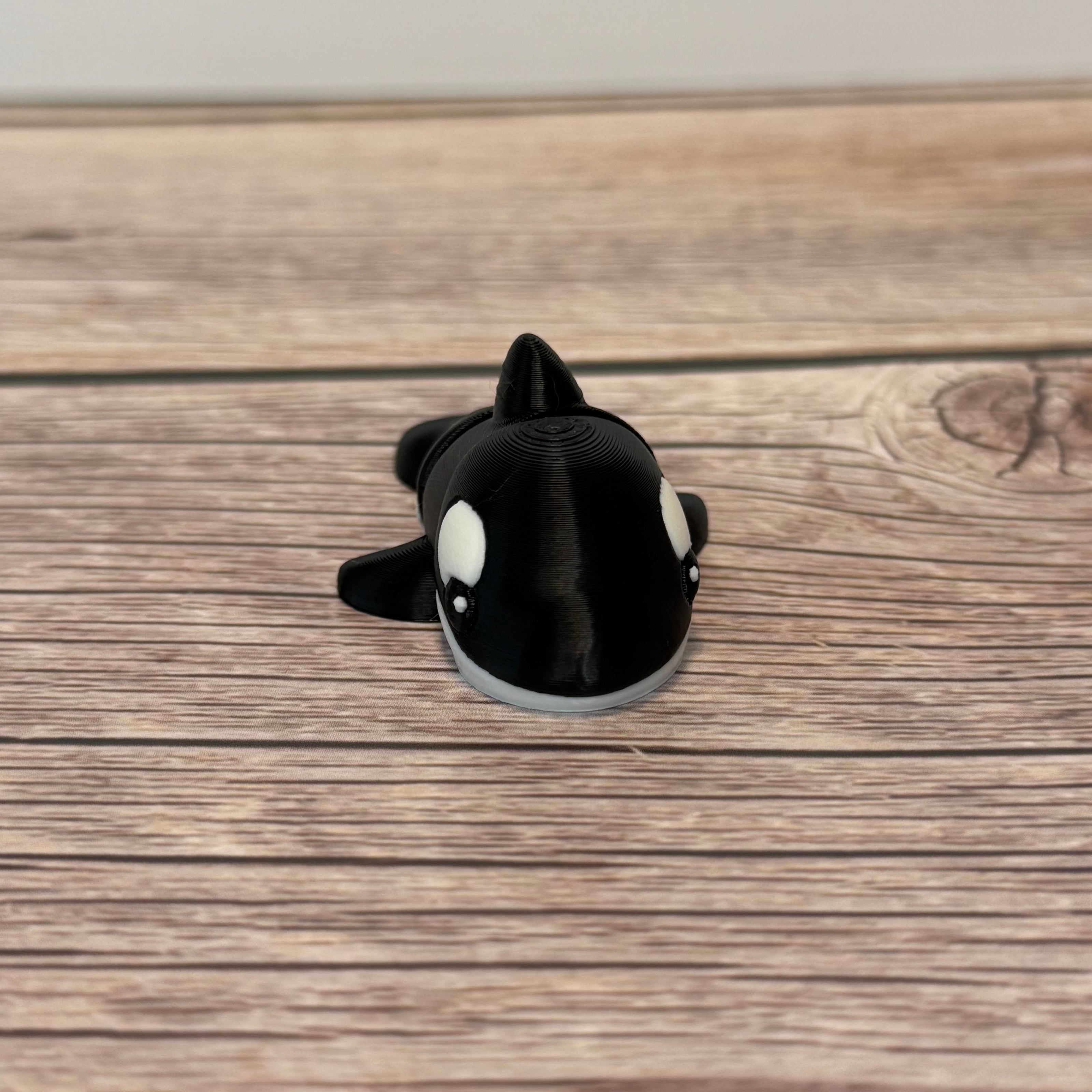 A small 3D printed black and white articulated mini orca toy placed on a wooden surface.