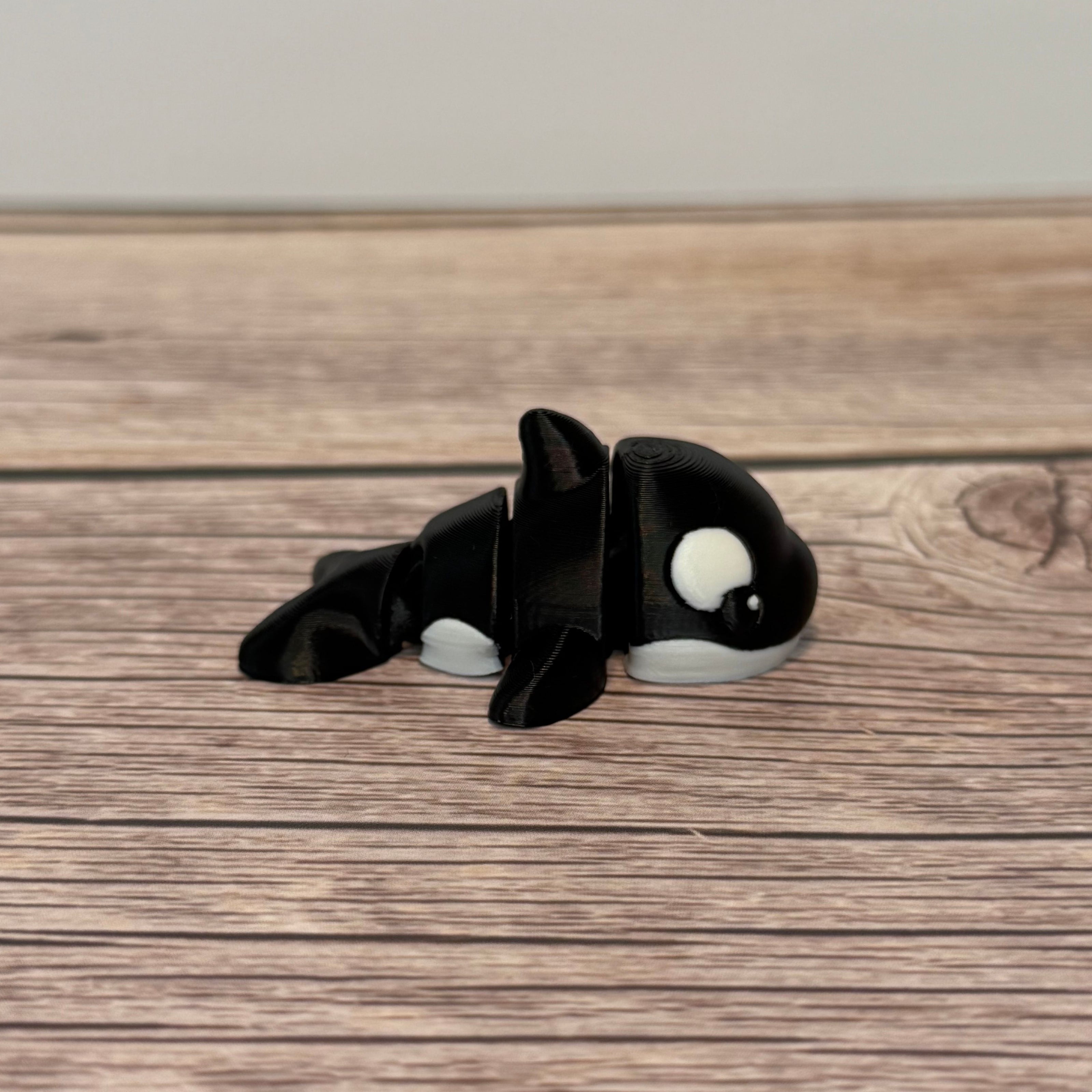 A small 3D printed black and white articulated mini orca toy placed on a wooden surface.