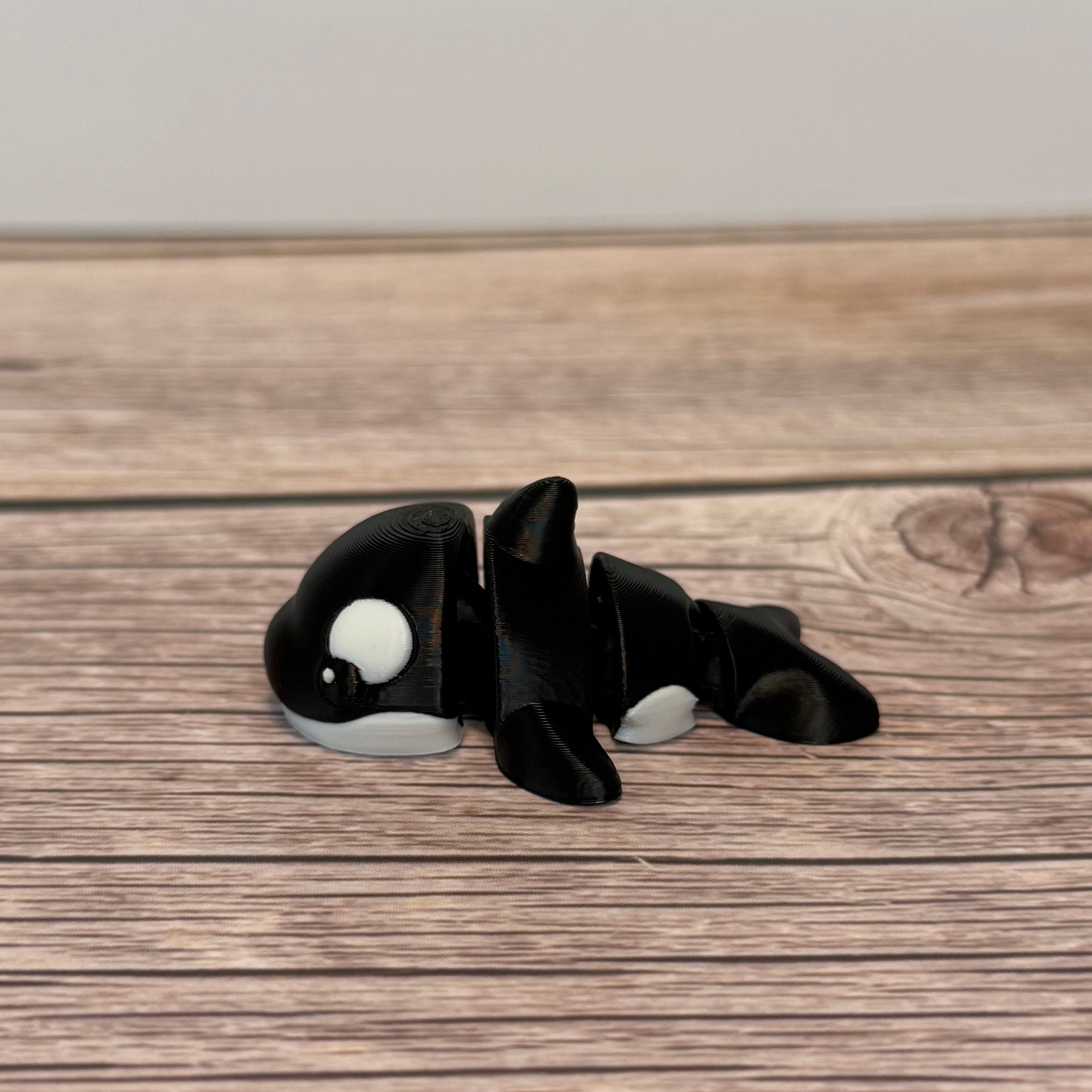 A small 3D printed black and white articulated mini orca toy placed on a wooden surface.