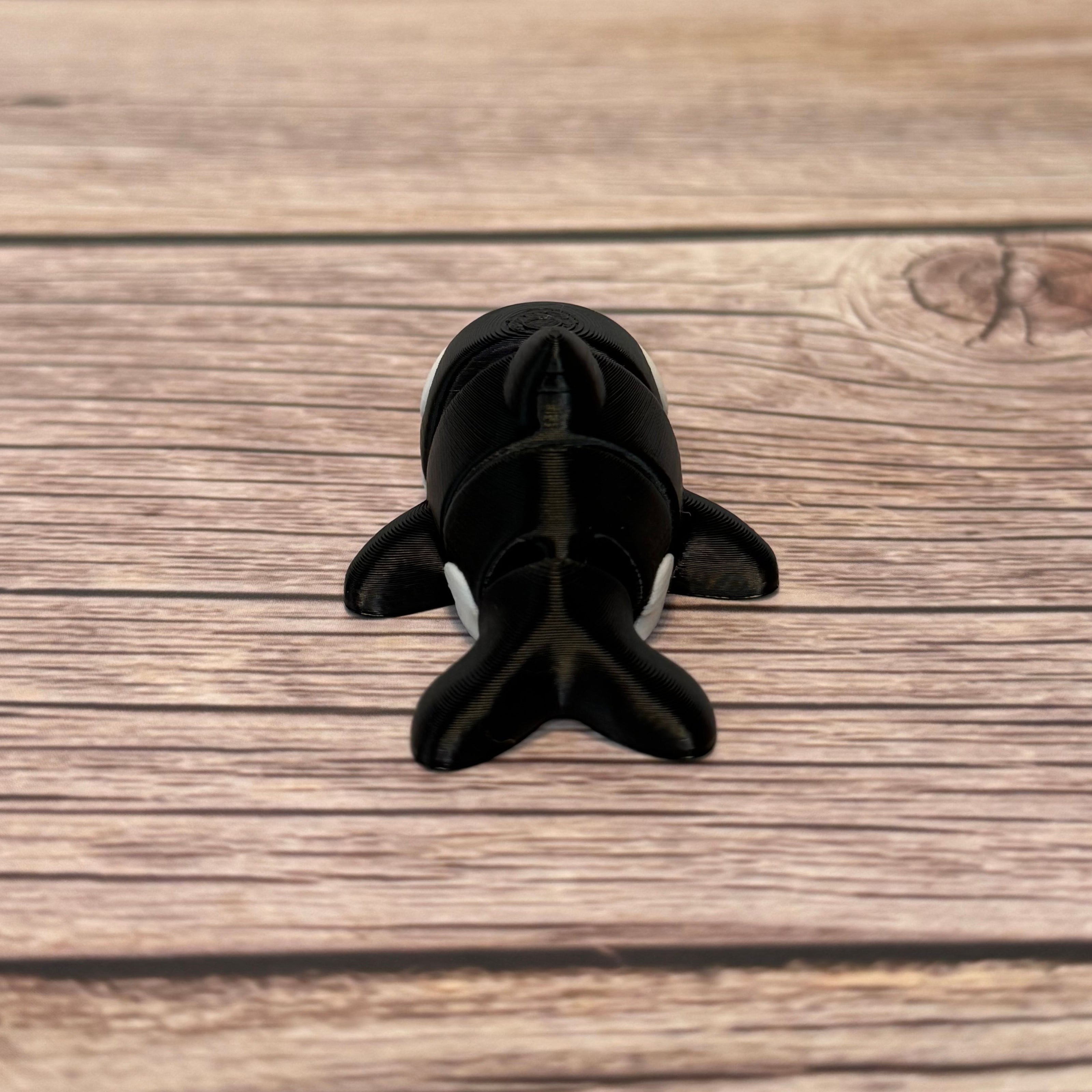 A small 3D printed black and white articulated mini orca toy placed on a wooden surface.
