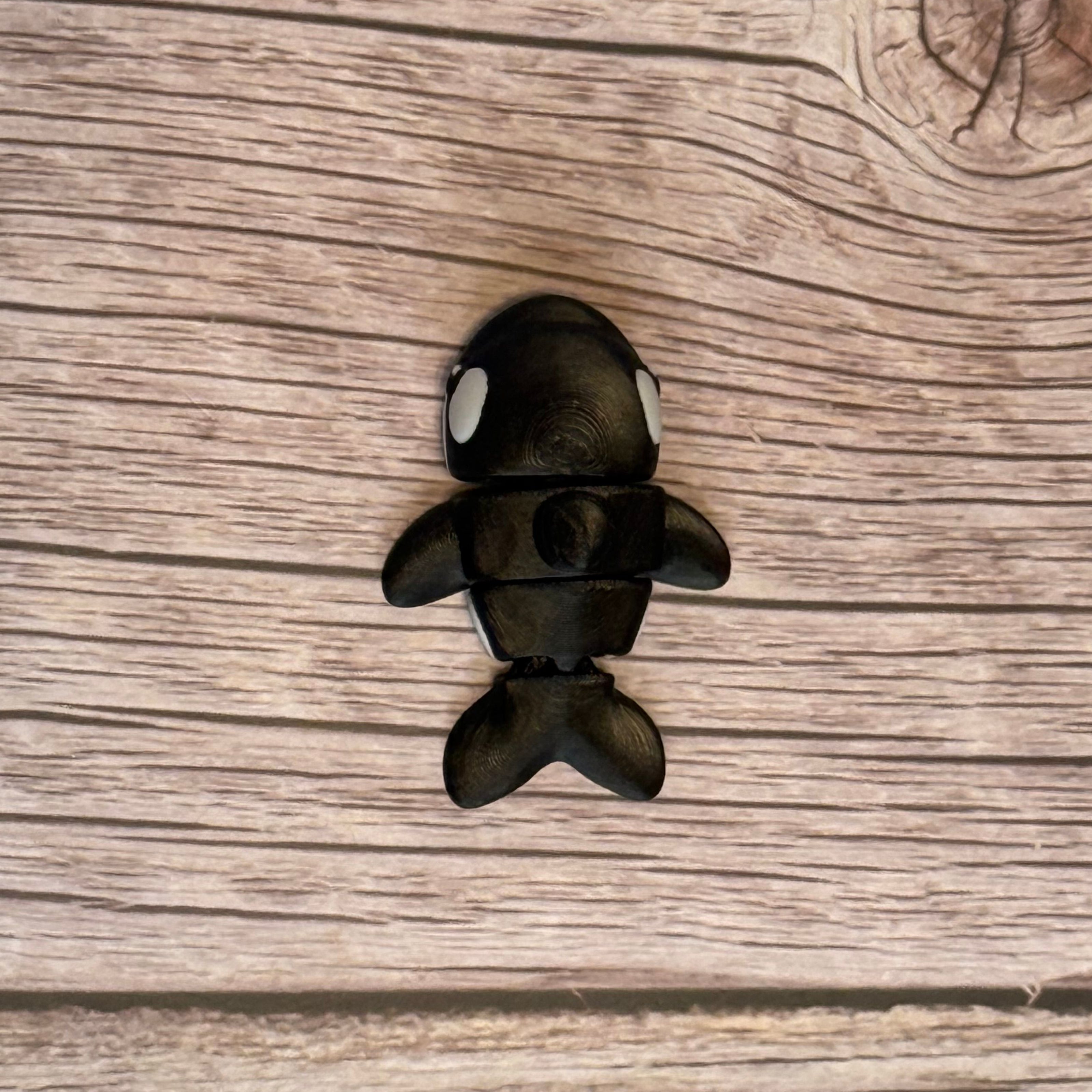 A small 3D printed black and white articulated mini orca toy placed on a wooden surface.
