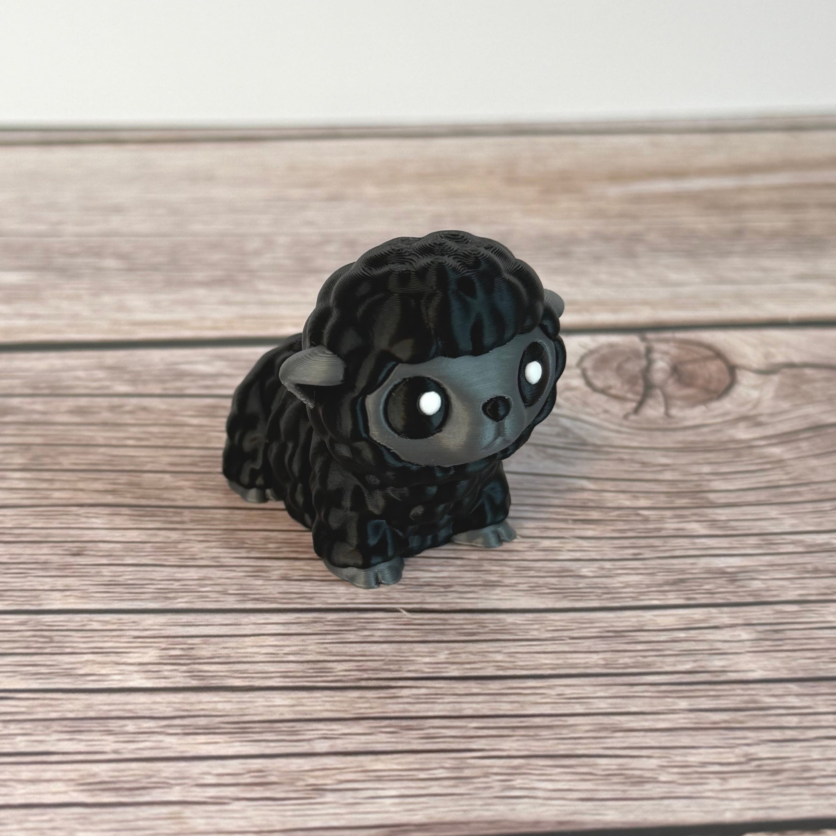 3D-printed articulated black and gray sheep figurine place on a wooden surface with white background