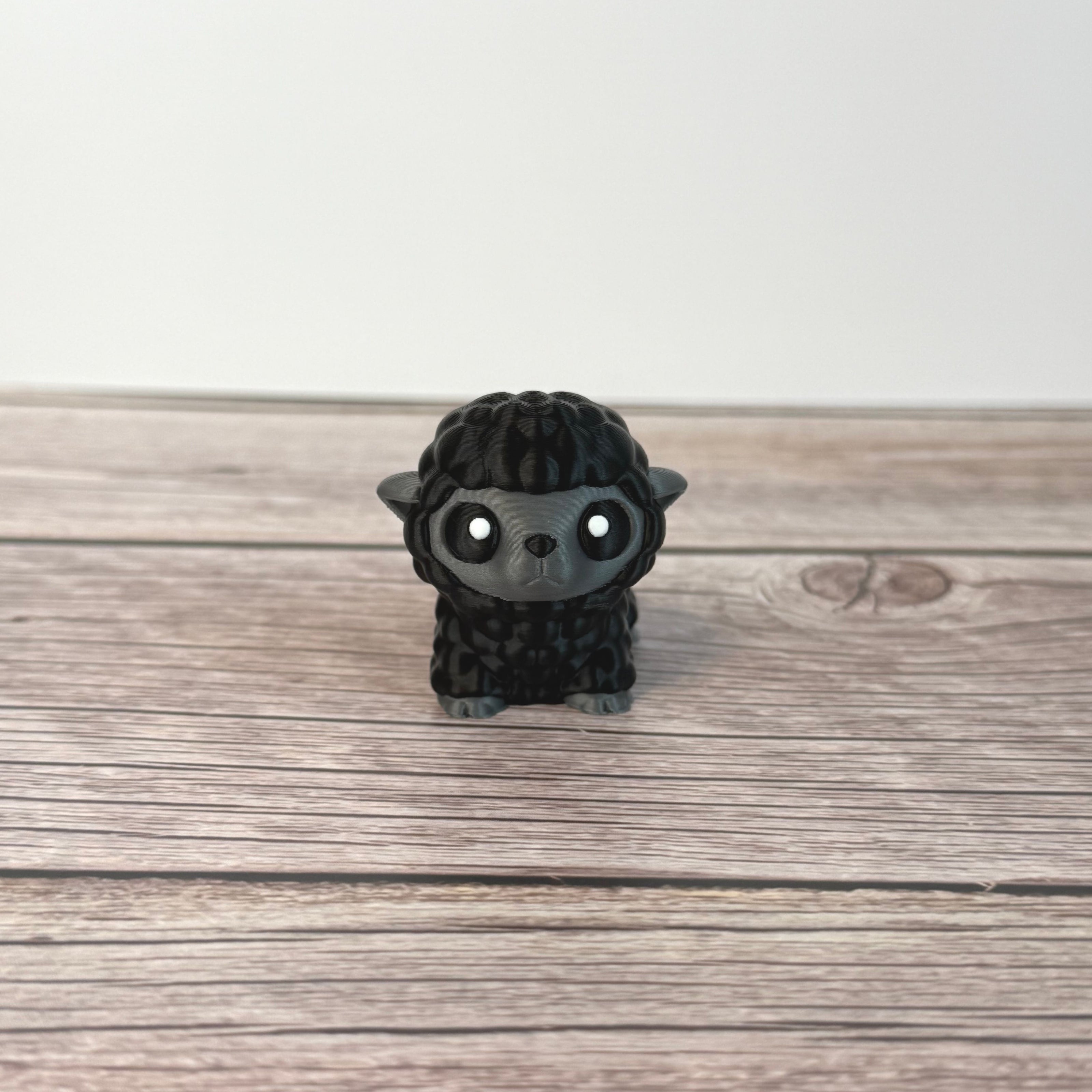 3D-printed articulated black and gray sheep figurine place on a wooden surface with white background
