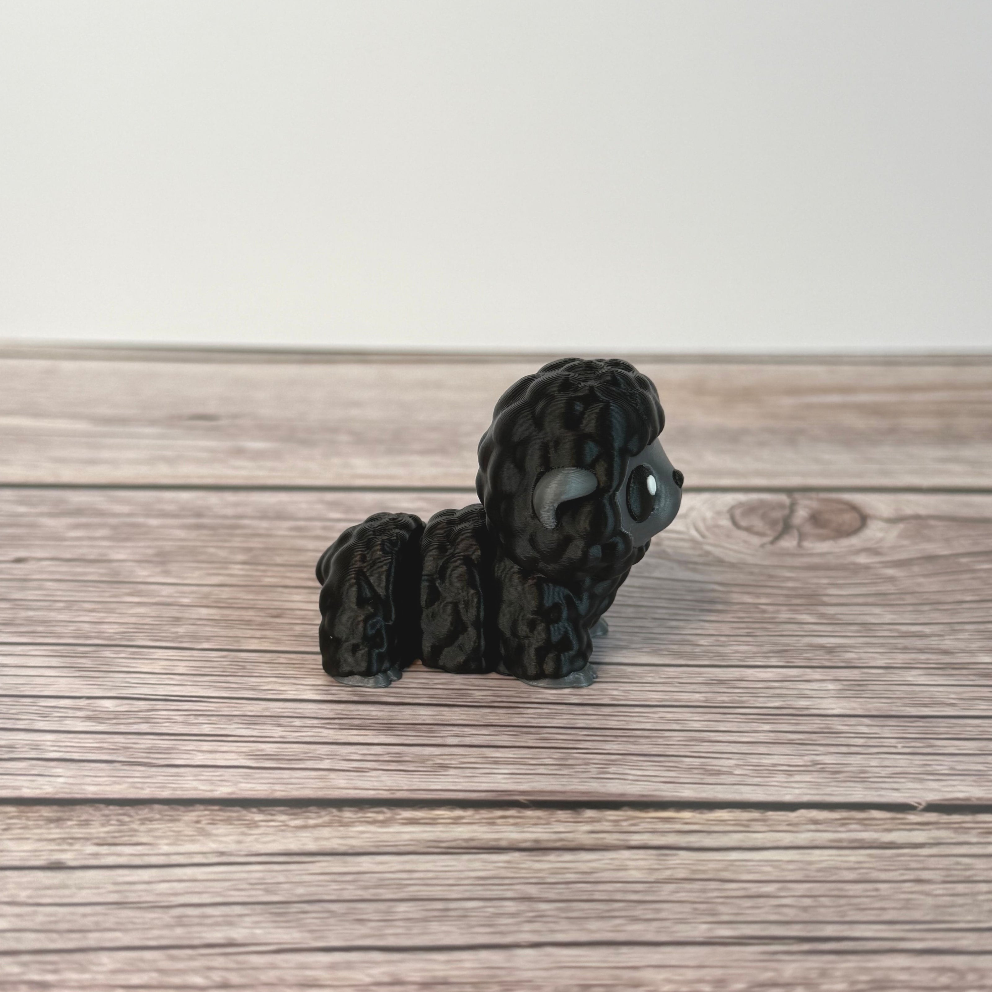 3D-printed articulated black and gray sheep figurine place on a wooden surface with white background