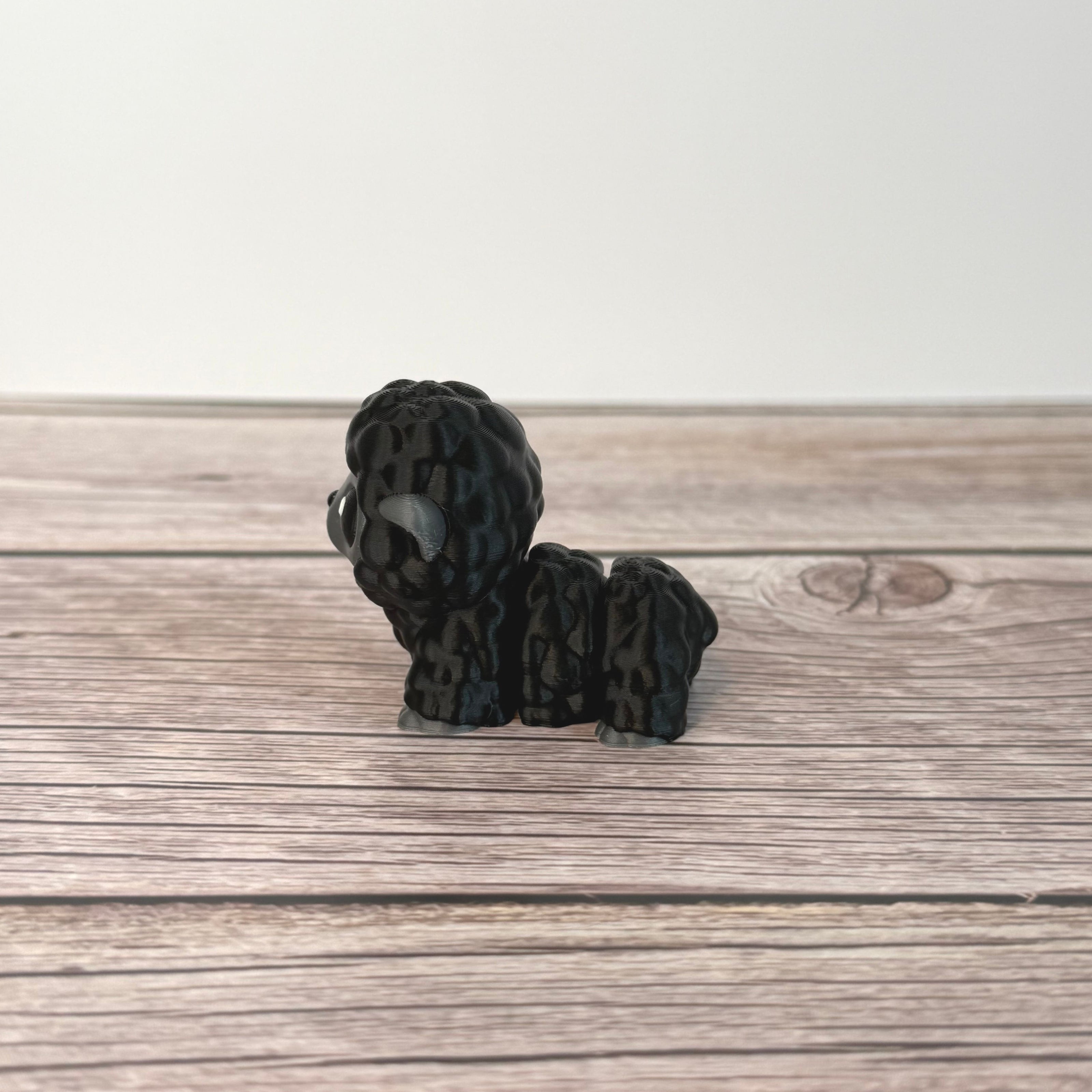 3D-printed articulated black and gray sheep figurine place on a wooden surface with white background