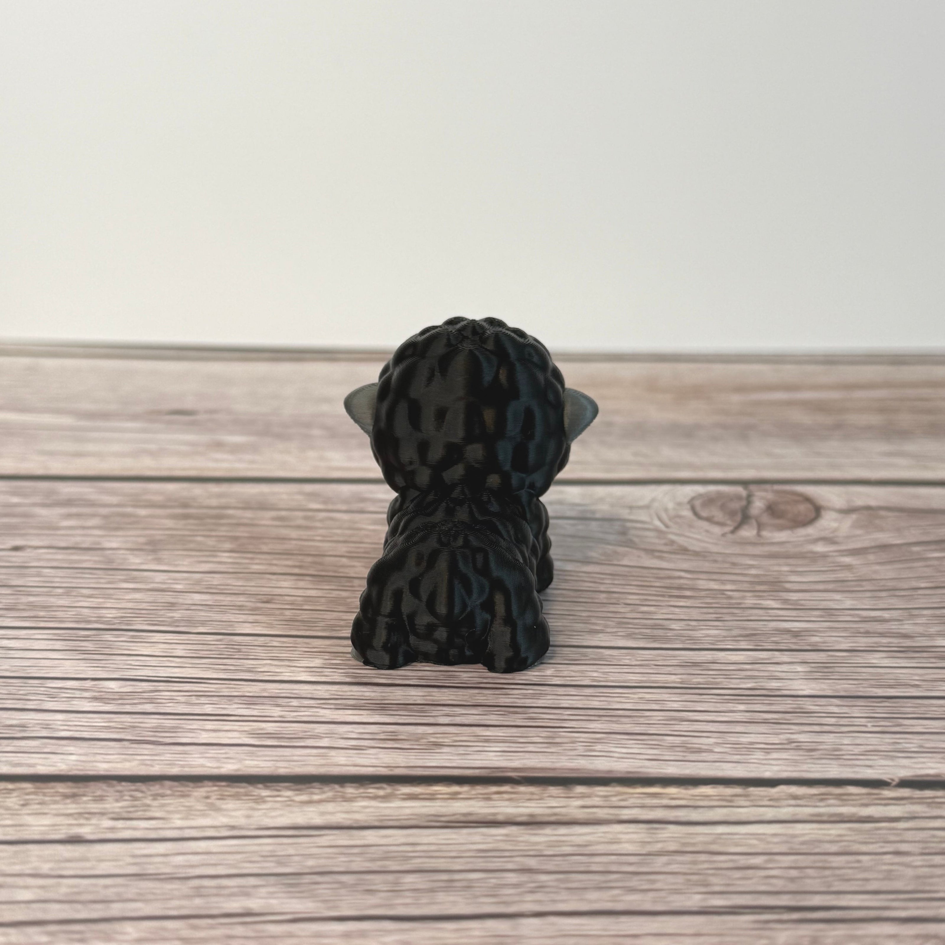 3D-printed articulated black and gray sheep figurine place on a wooden surface with white background