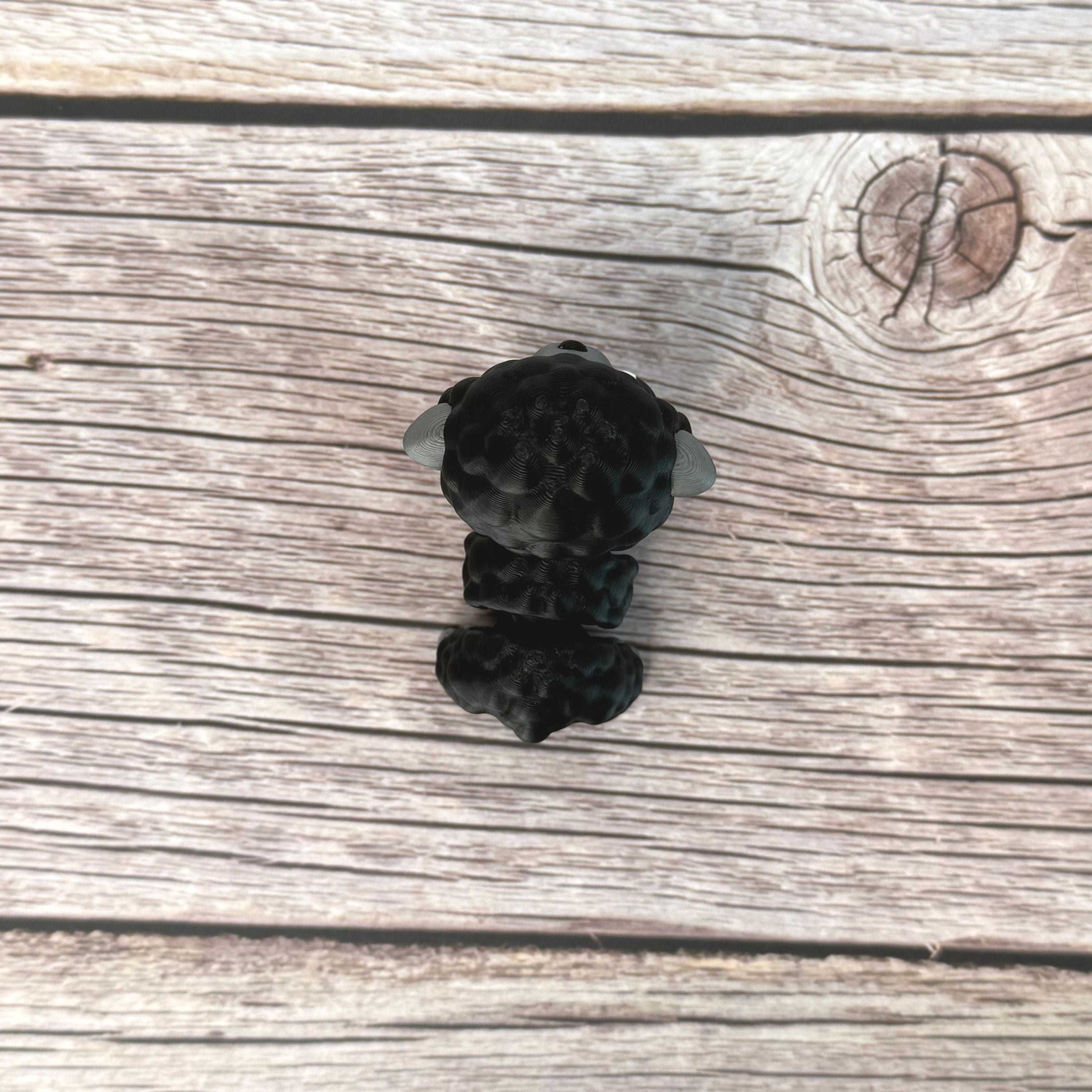3D-printed articulated black and gray sheep figurine place on a wooden surface 