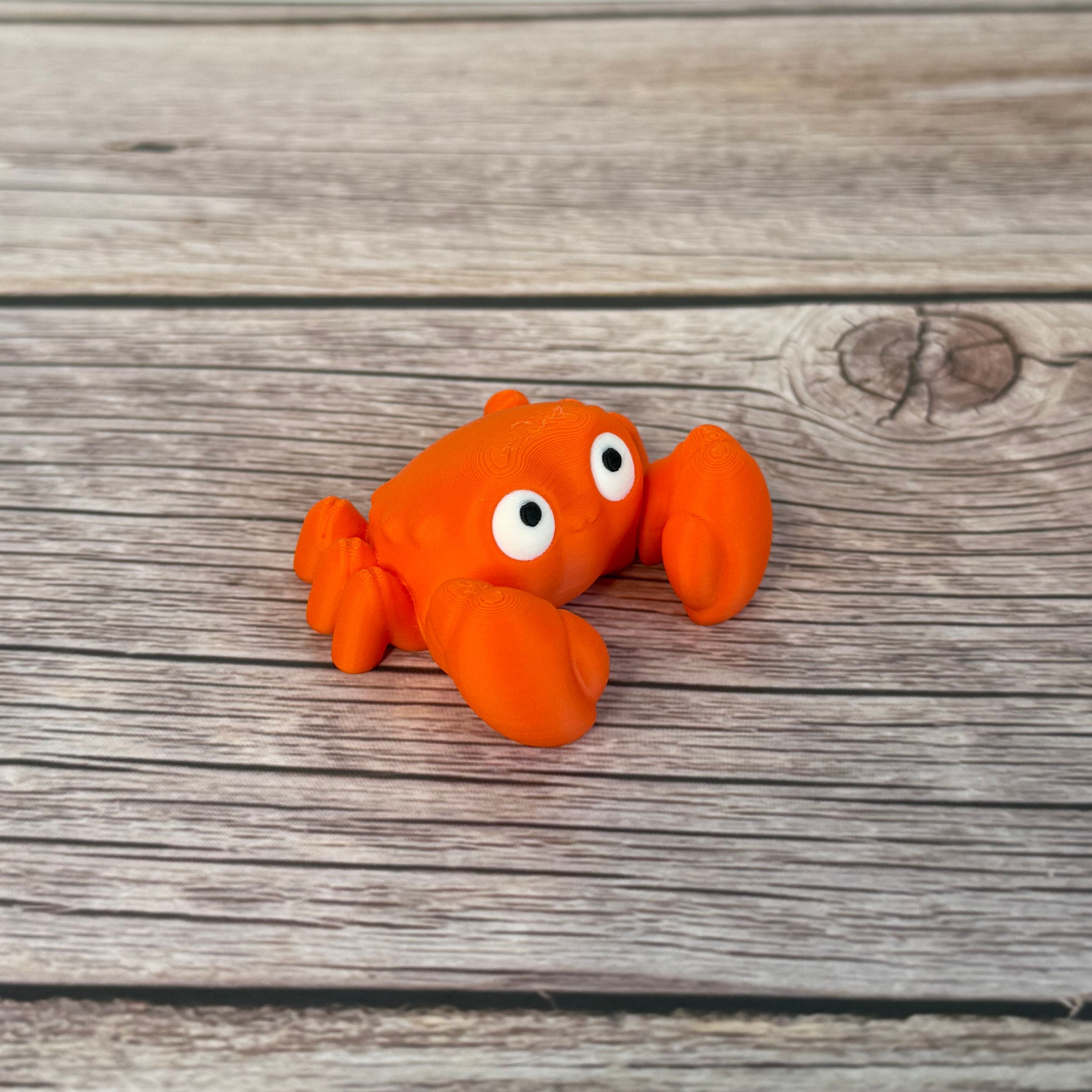 A small orange articulated mini crab toy with movable claws, placed on a wooden surface.