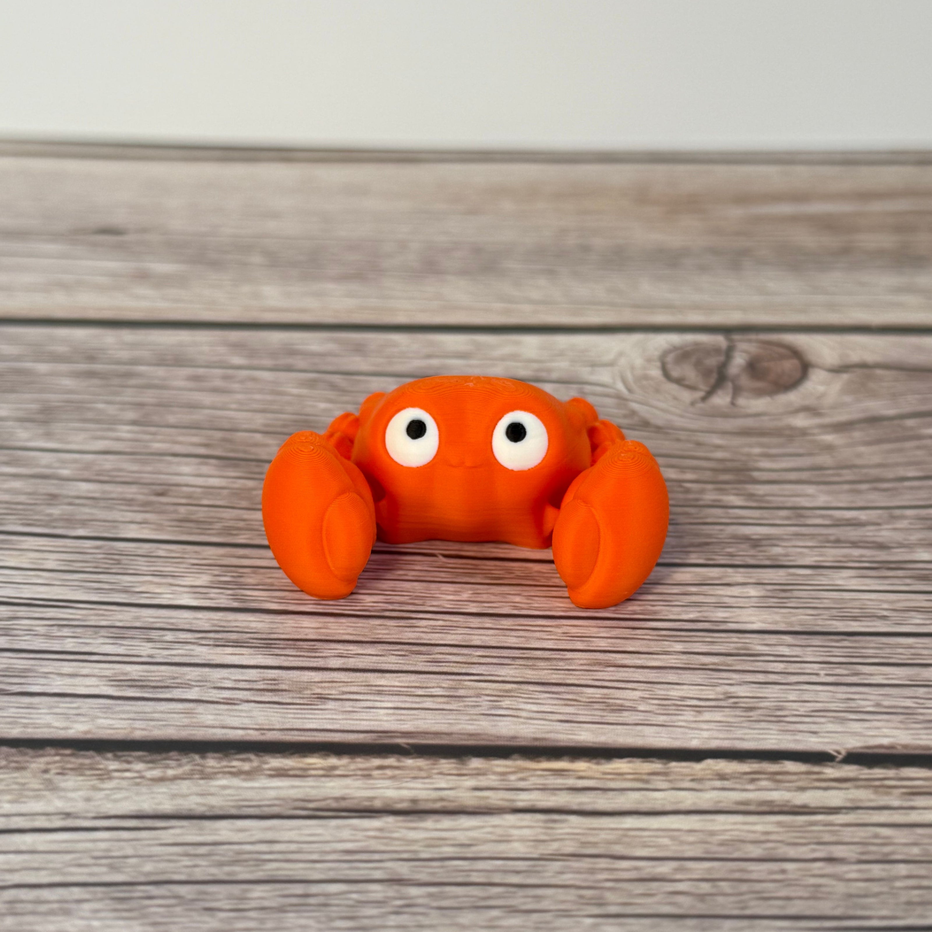 A small orange articulated mini crab toy with movable claws, placed on a wooden surface.
