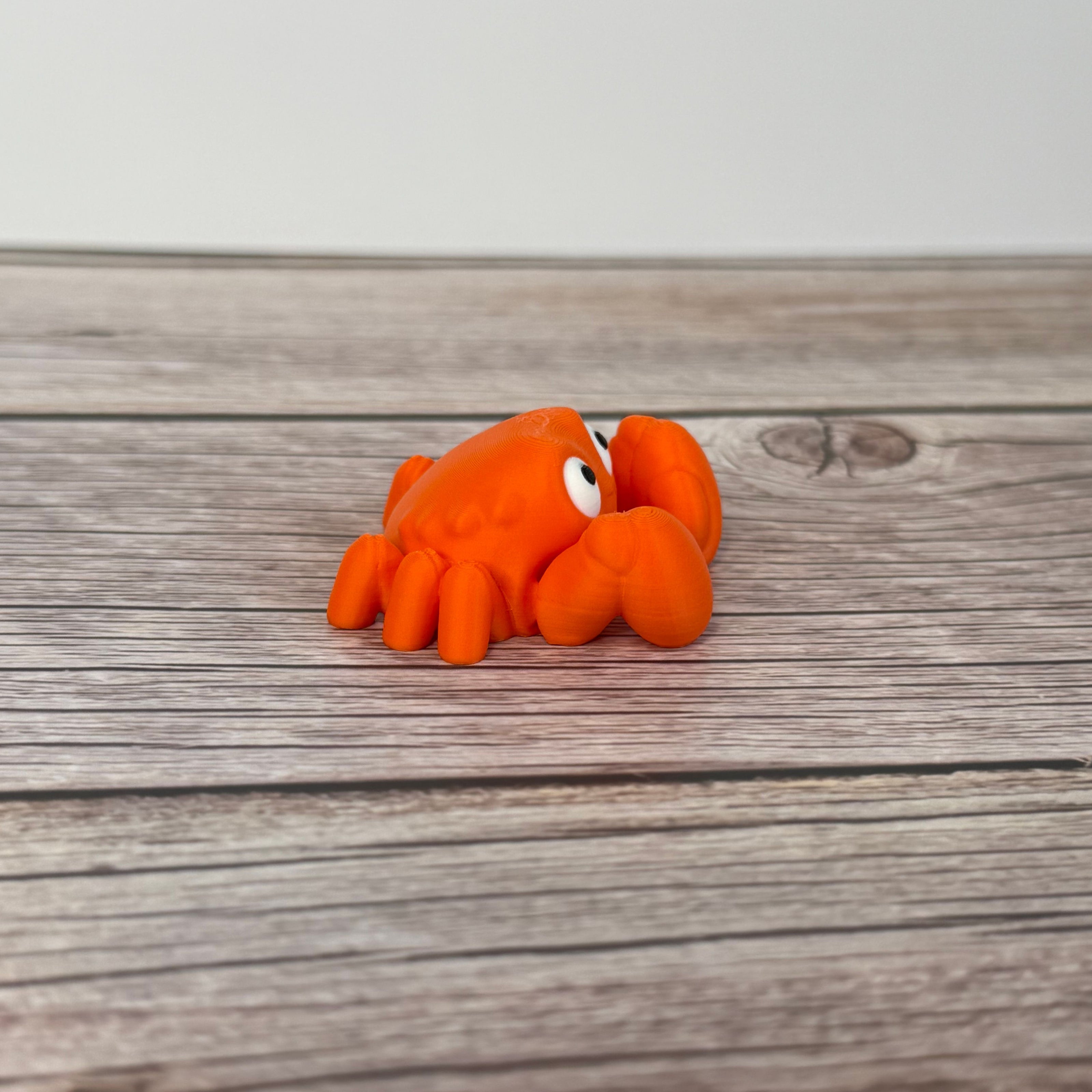 A small orange articulated mini crab toy with movable claws, placed on a wooden surface.