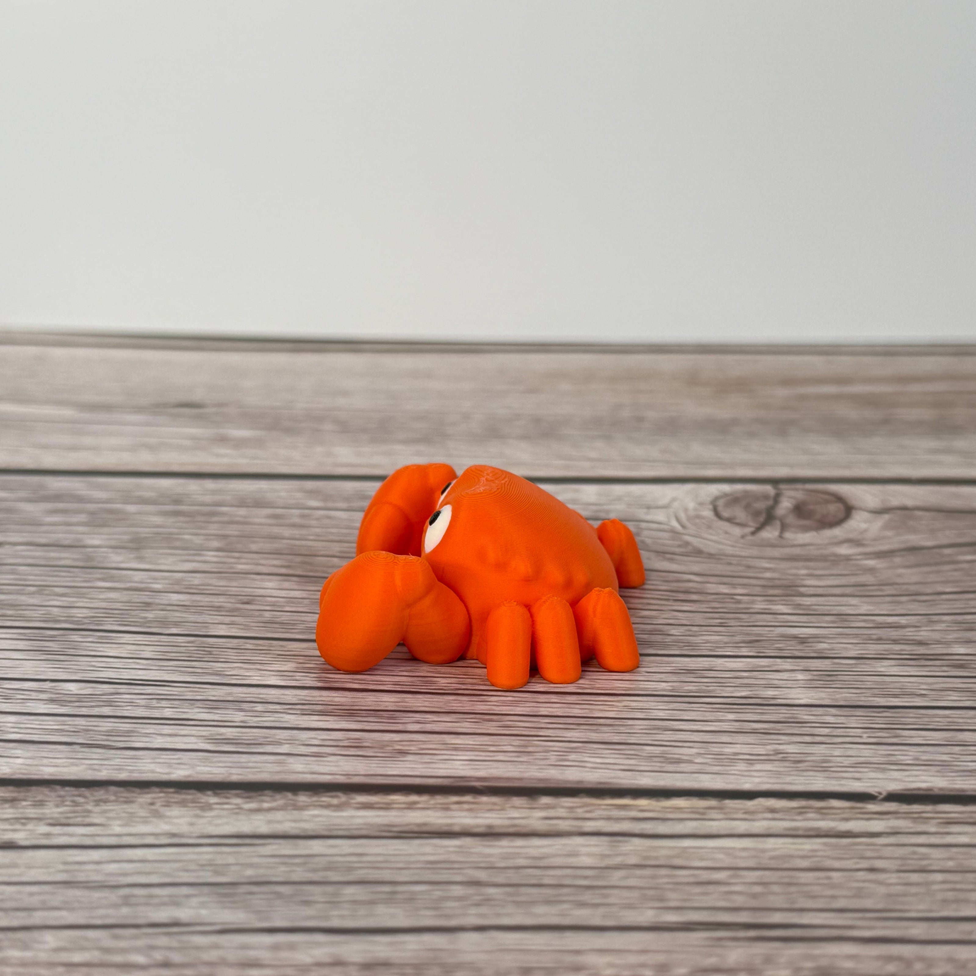 A small orange articulated mini crab toy with movable claws, placed on a wooden surface.
