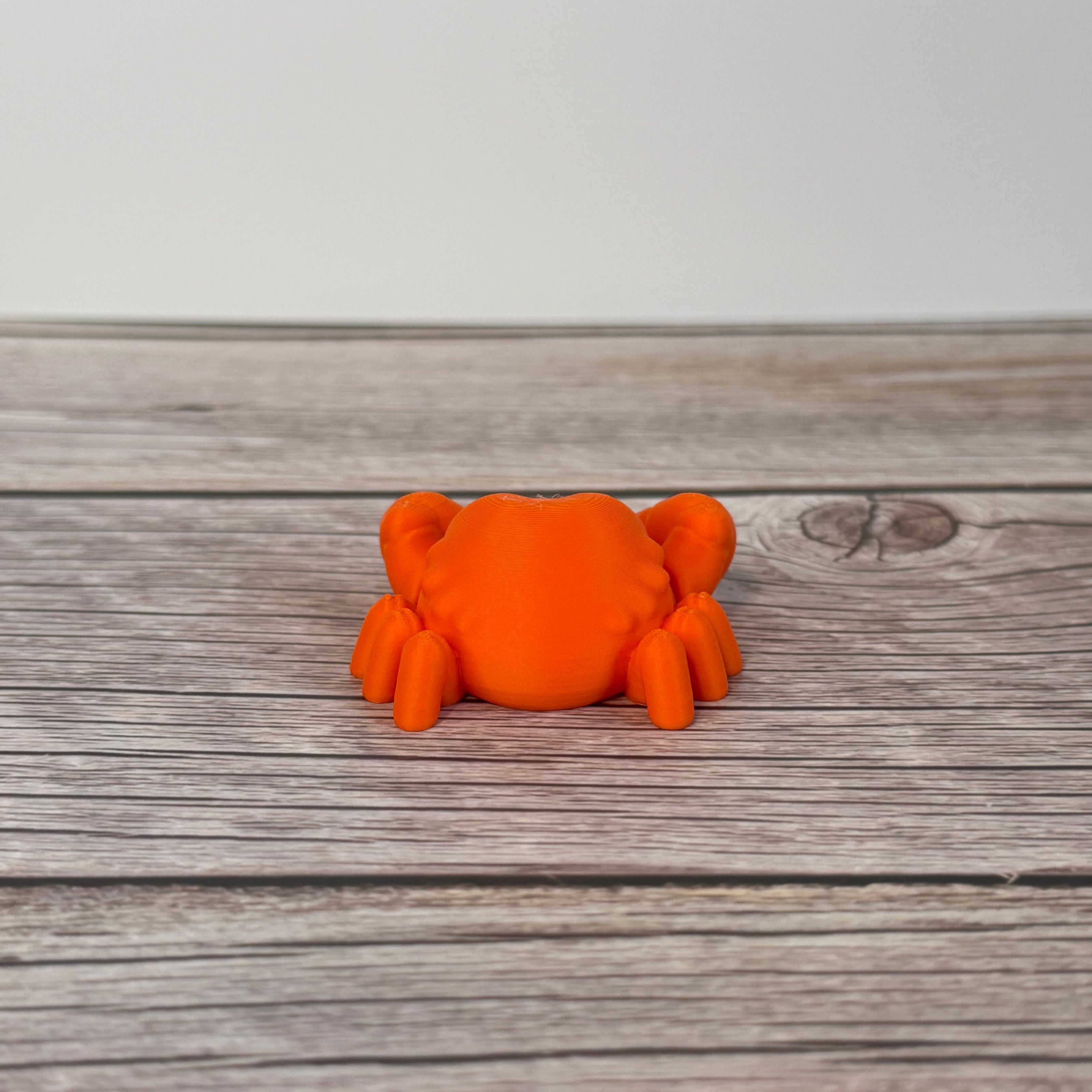 A small orange articulated mini crab toy with movable claws, placed on a wooden surface.