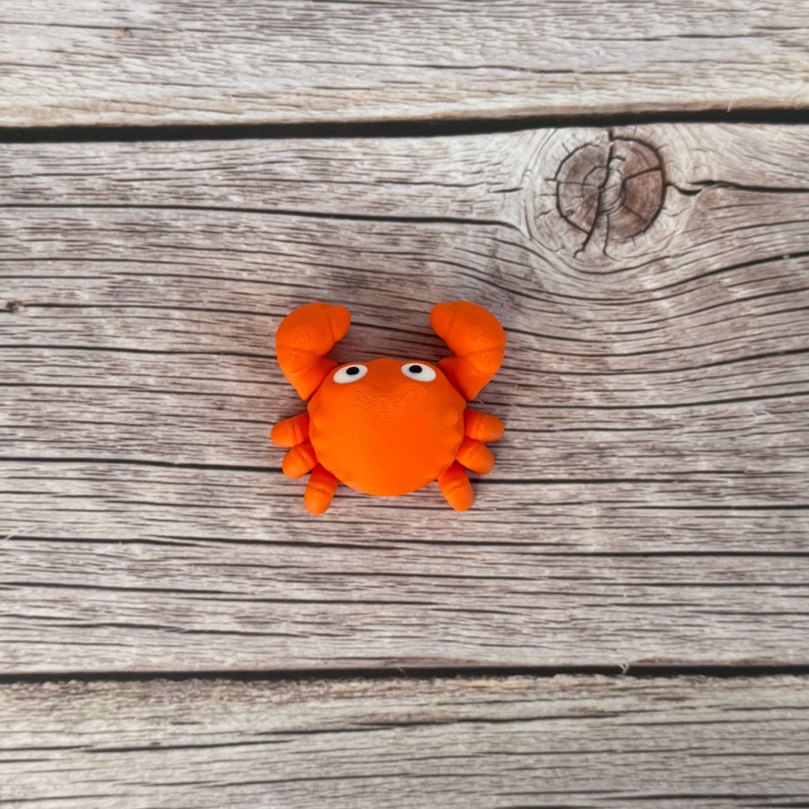 A small orange articulated mini crab toy with movable claws, placed on a wooden surface.