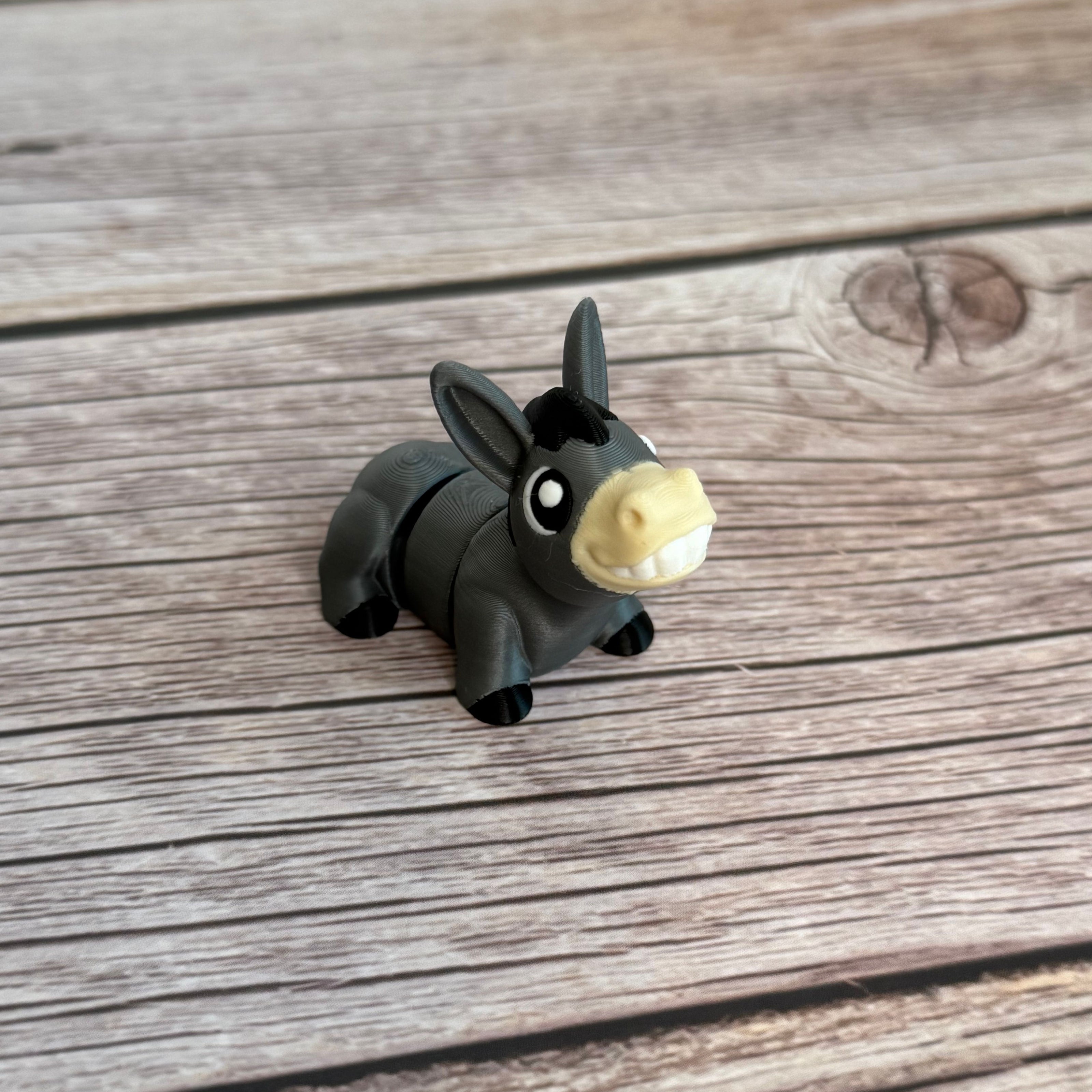 A small 3D printed gray donkey toy with movable segments, positioned on a wooden surface.