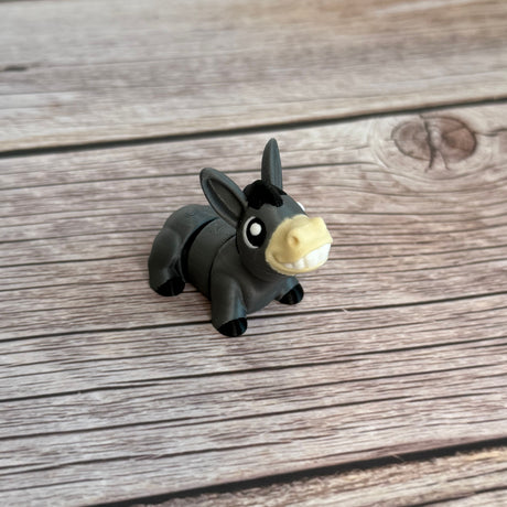 A small 3D printed gray donkey toy with movable segments, positioned on a wooden surface.